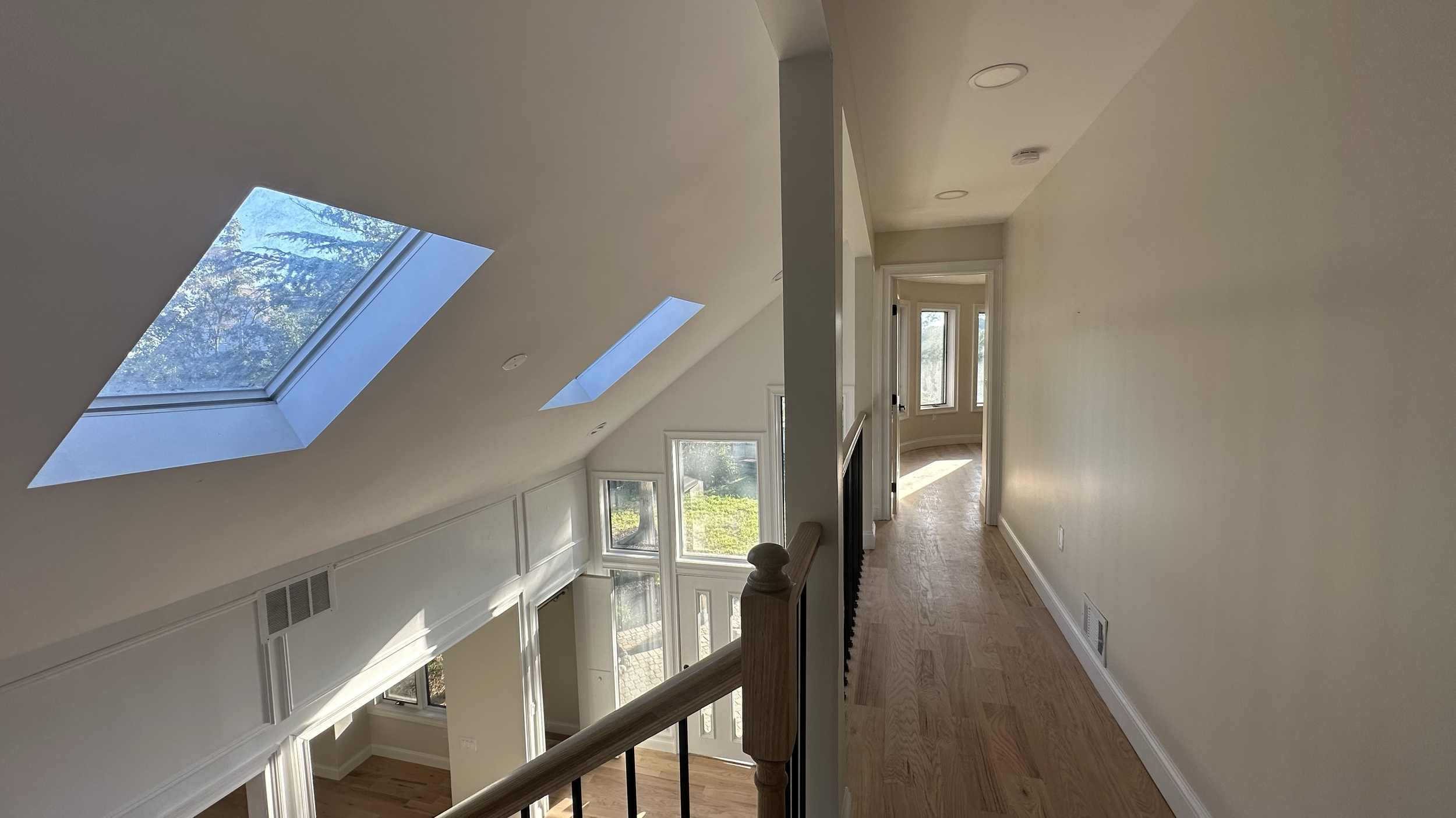 Interior of a house with a hallway leading to a sunroom with large windows and two skylights in the ceiling, and a staircase visible from the second floor.
