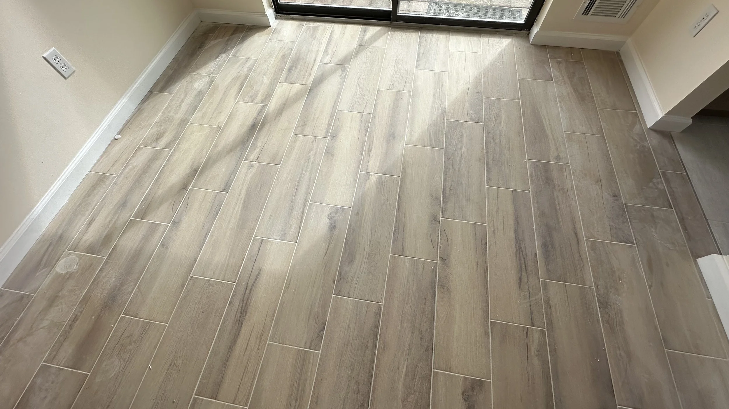 Interior room with beige tiled floor, light-colored walls, electrical outlets, and a glass sliding door leading to an outdoor area.