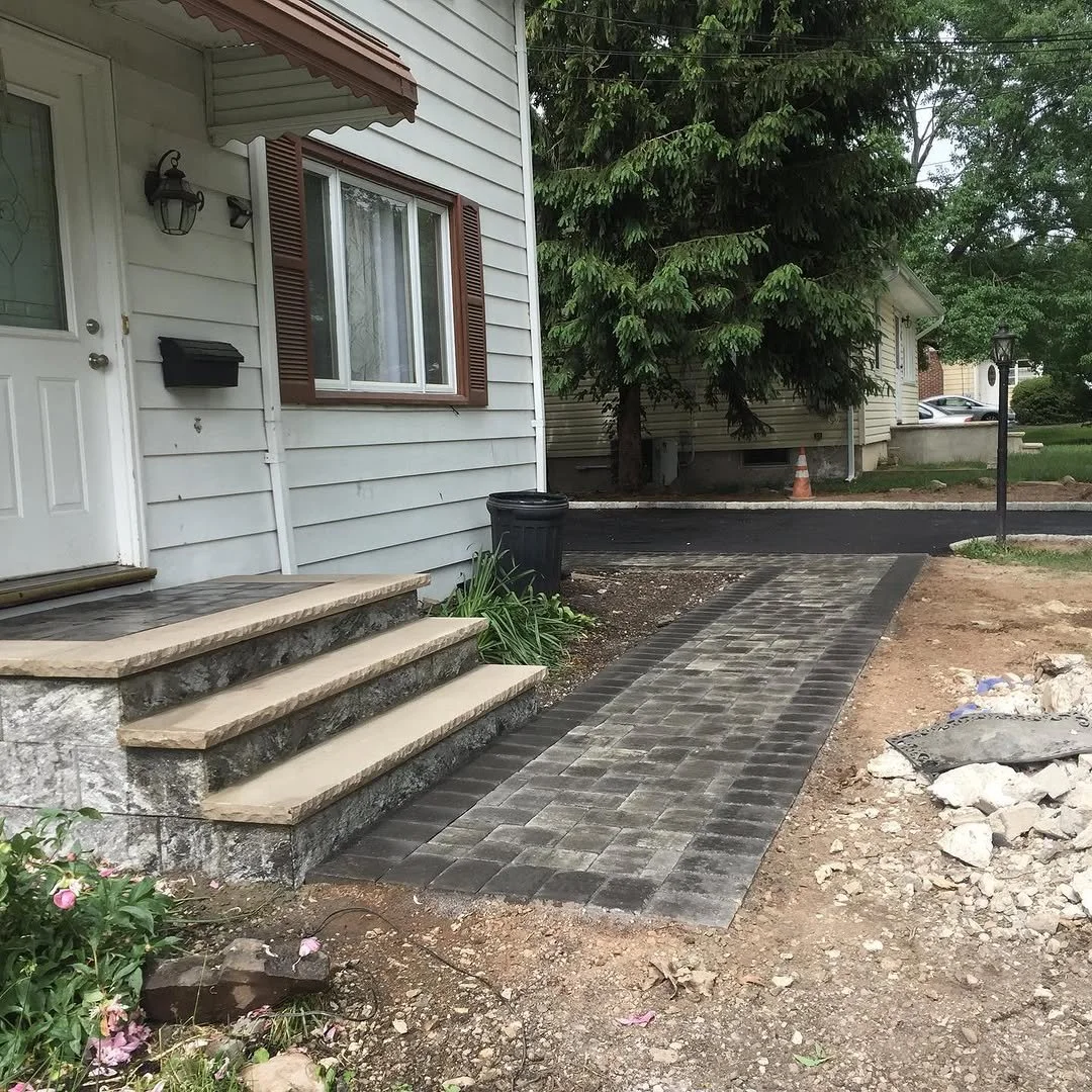 Front porch with steps, a new stone and paver walkway leading to a driveway, some construction work in progress, and a tree in the background.