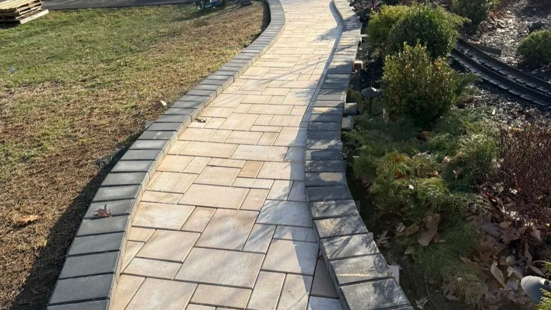Curved paved walkway with stone border next to a garden bed and grass area.