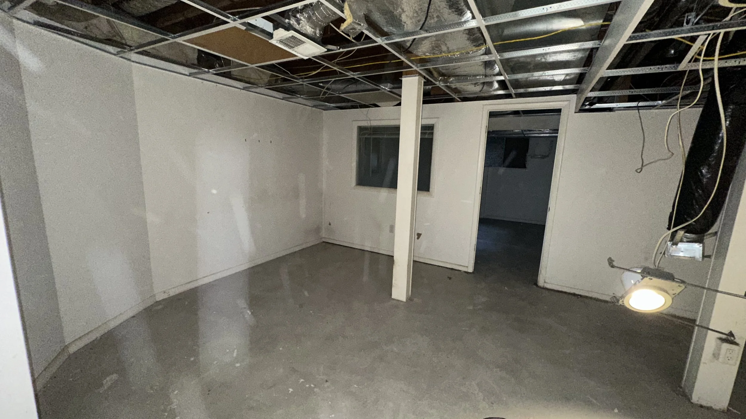 Empty room under renovation with unfinished walls, exposed ceiling wiring, and concrete floor.