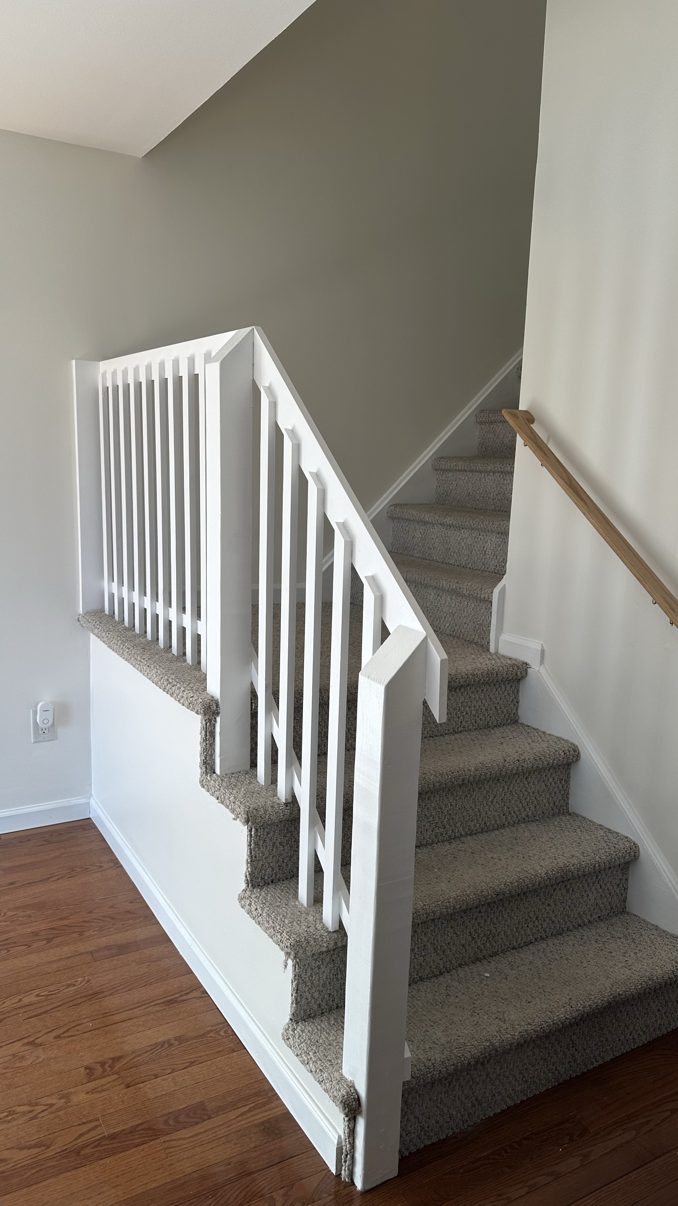 Carpeted staircase with a white railing and a wooden handrail, leading upstairs in a home interior.