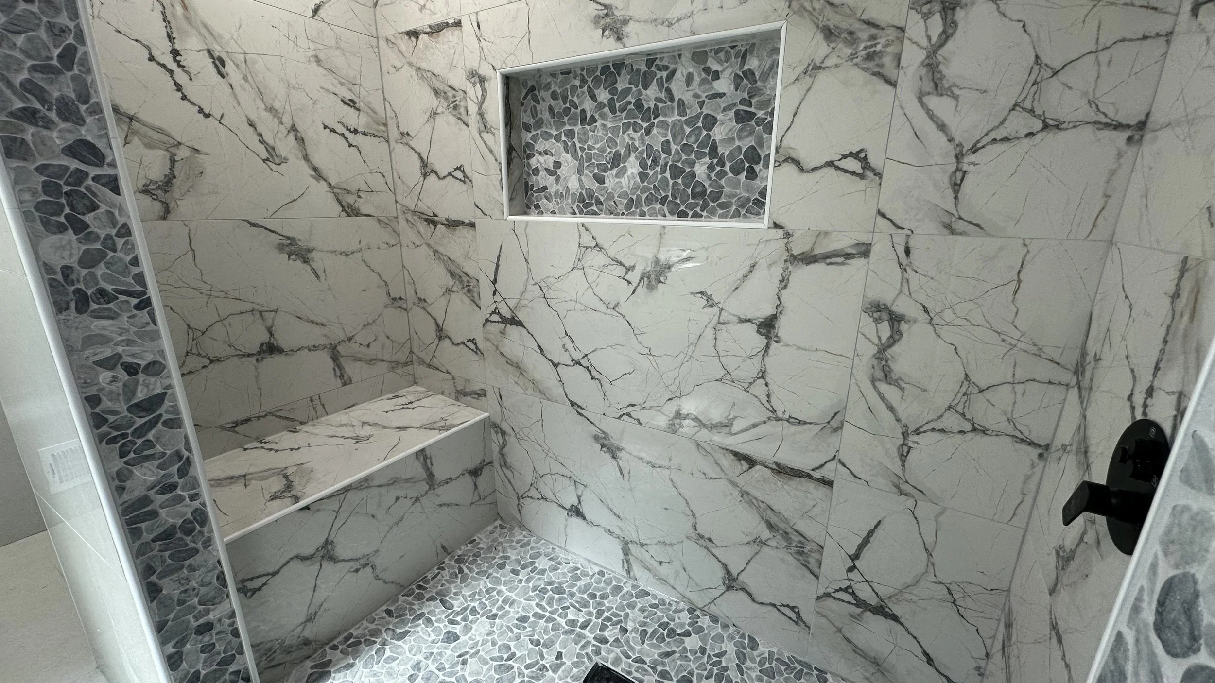 Marble tiled shower with a built-in bench, pebble floor, and a recessed pebble niche in the wall.