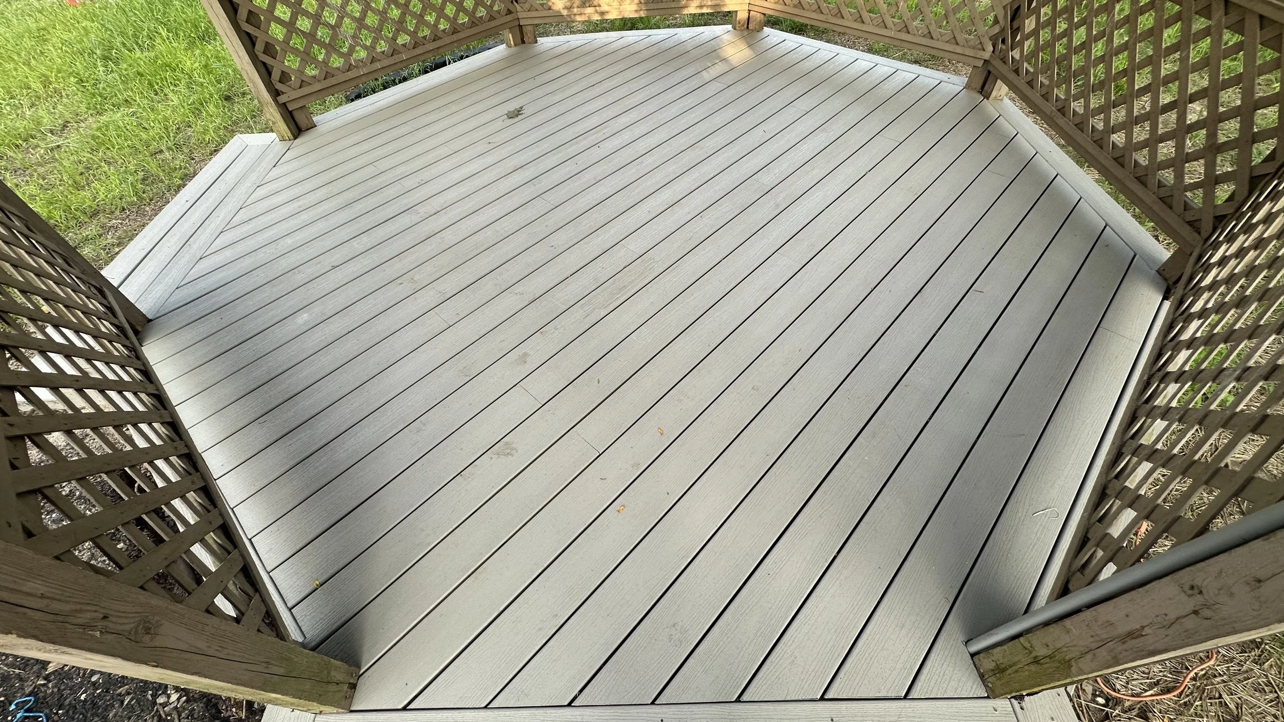 View of a small outdoor wooden deck with light gray planks and a lattice fence around it.