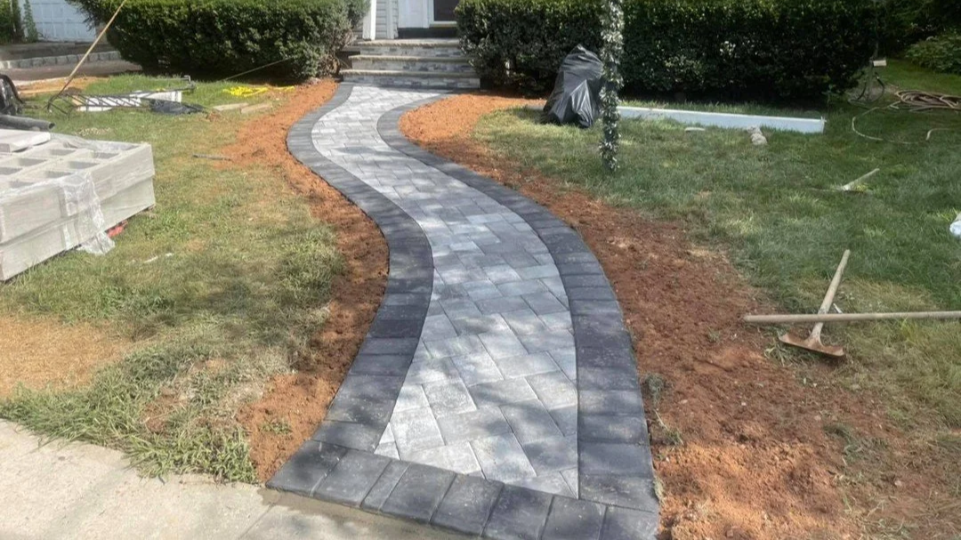 Curving walkway made of gray and black pavers under construction in front yard of house.