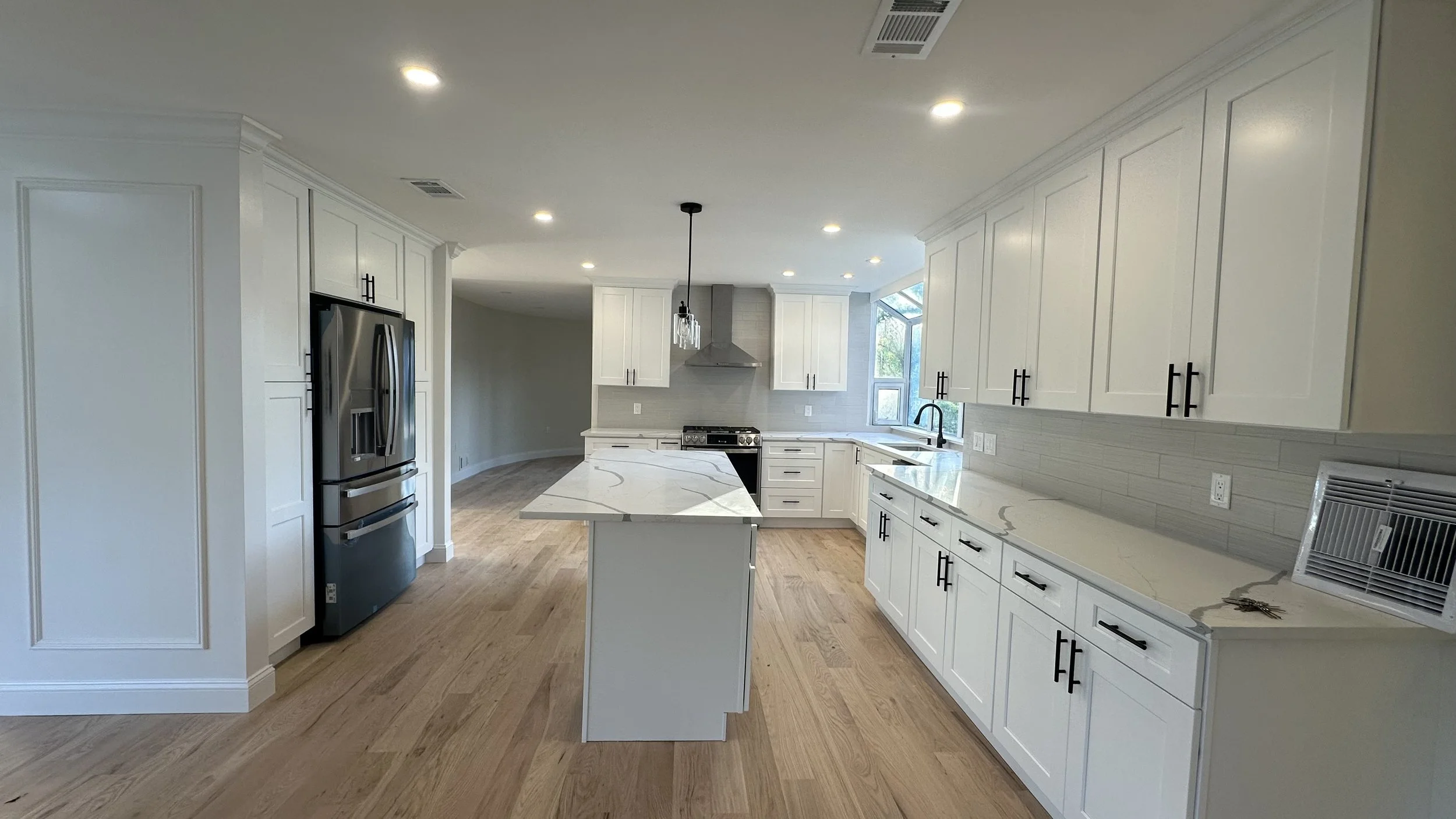 Modern kitchen with white cabinets, marble countertops, stainless steel appliances, hardwood floors, and a breakfast bar with an island. Picture shows upper and lower cabinets, a stainless steel oven, a range hood, a refrigerator, and a window near the sink.