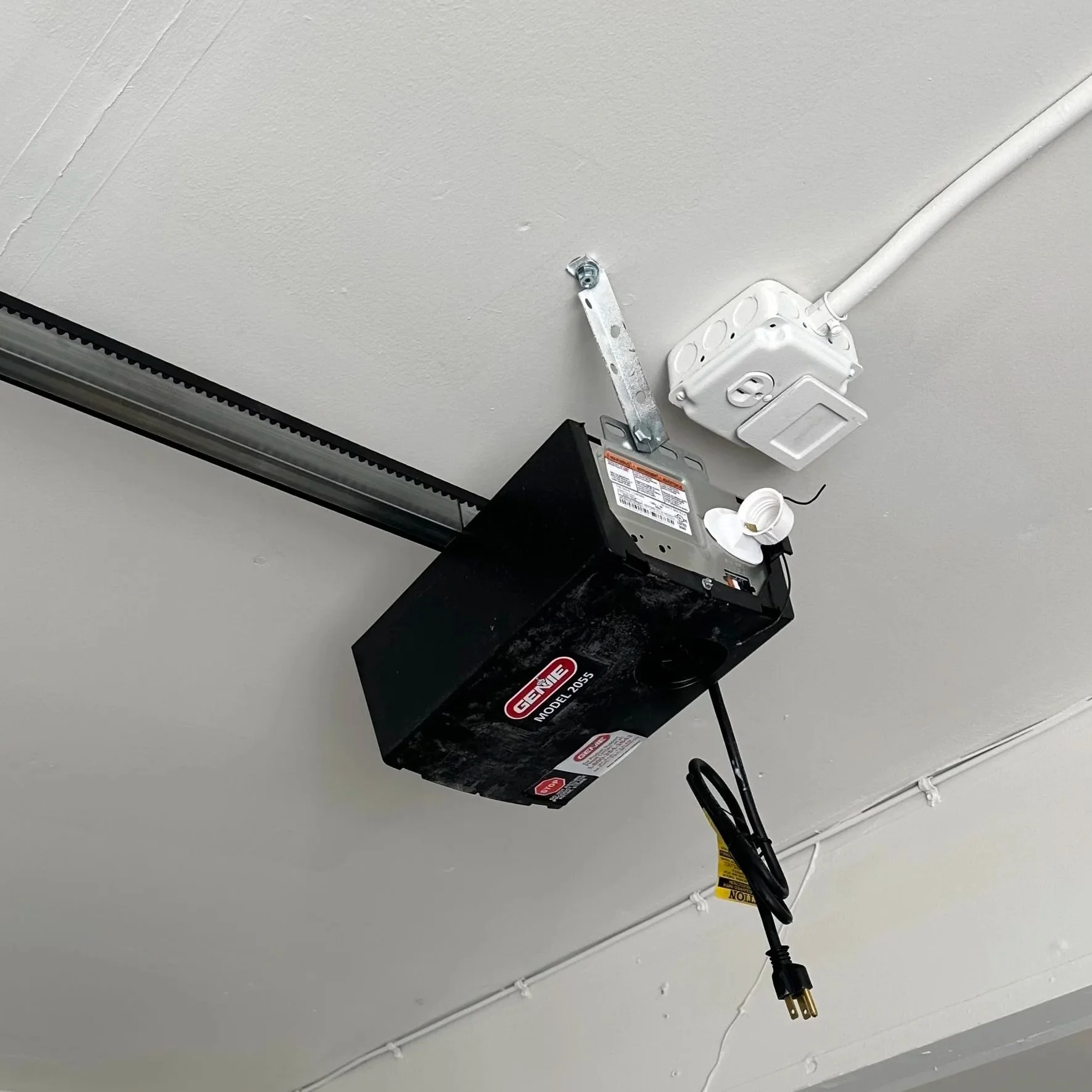 Garage door opener mounted on ceiling with power cord hanging down.