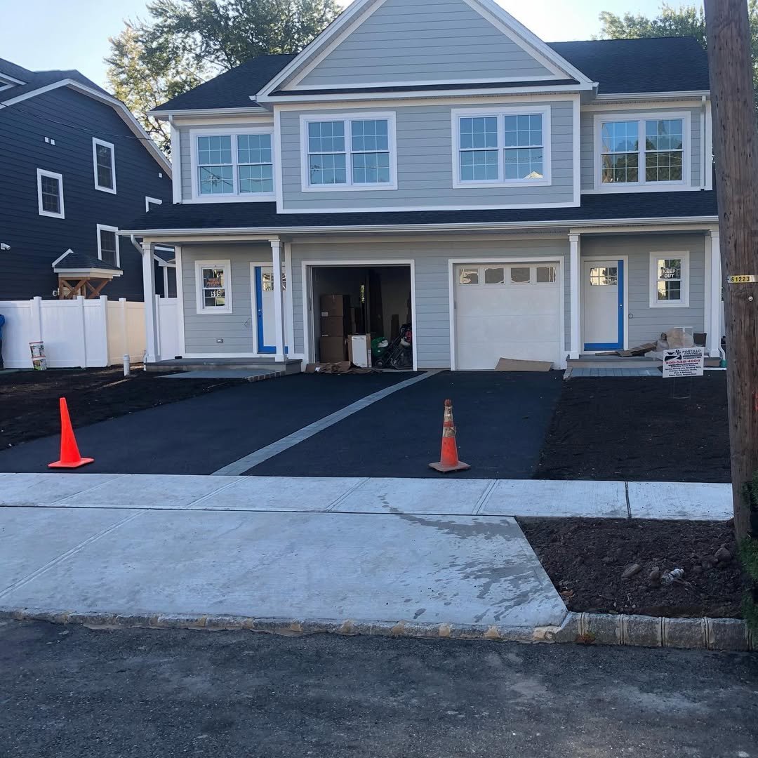 A two-story house under construction with a garage and driveway, orange traffic cones, and construction materials in the yard.