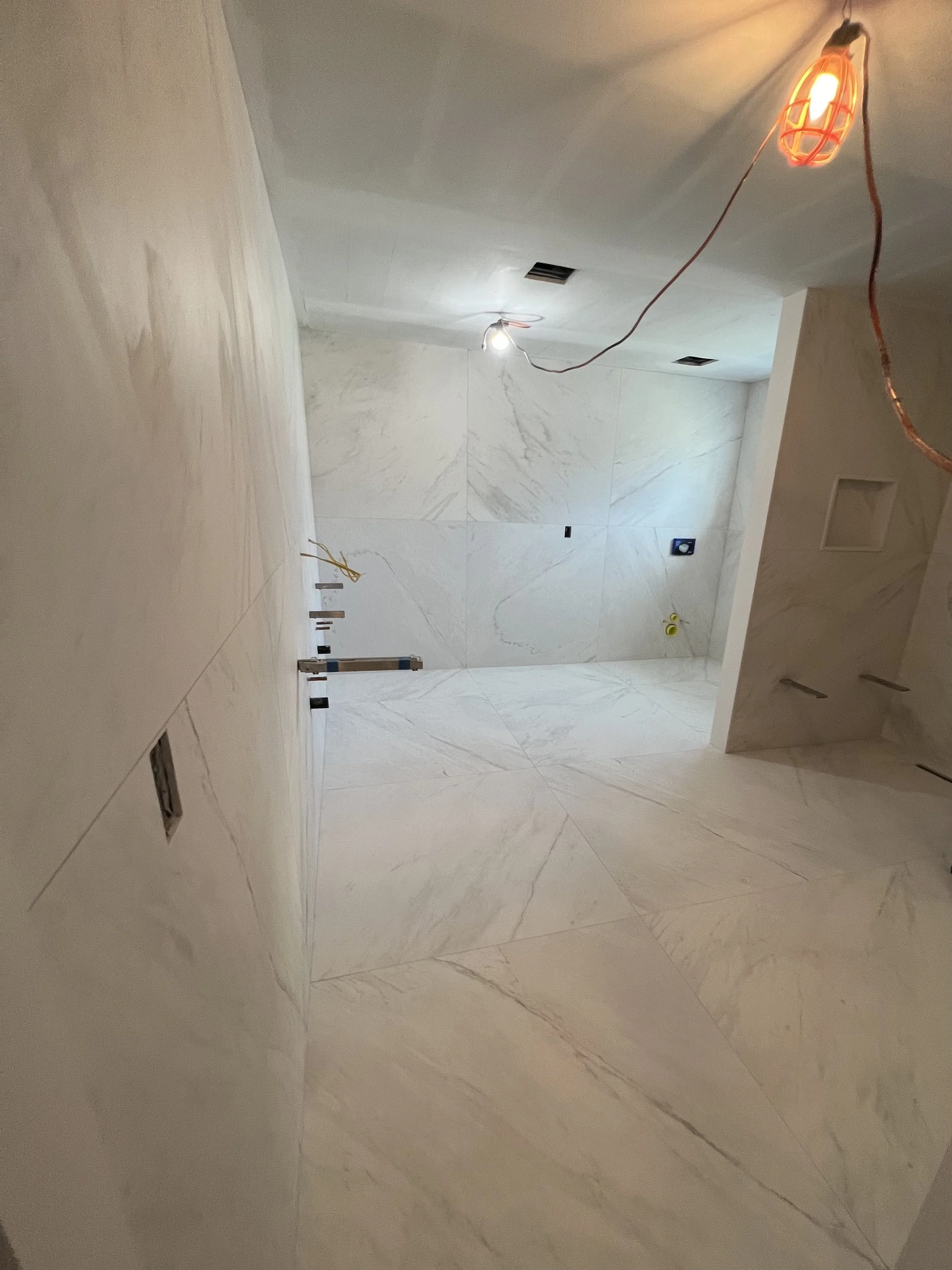 Interior room with white marble walls and floor, temporary construction lighting, and electrical outlets visible.