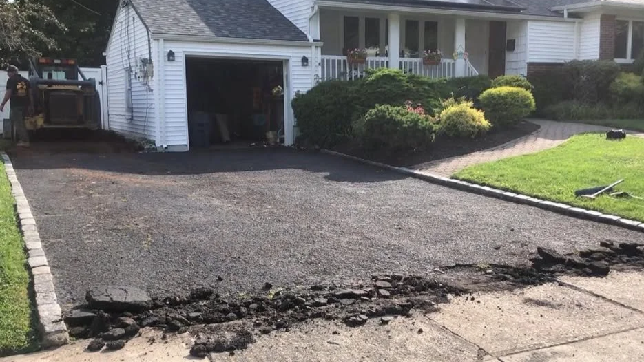 A driveway in front of a suburban house under renovation, with asphalt partially removed and construction tools nearby.