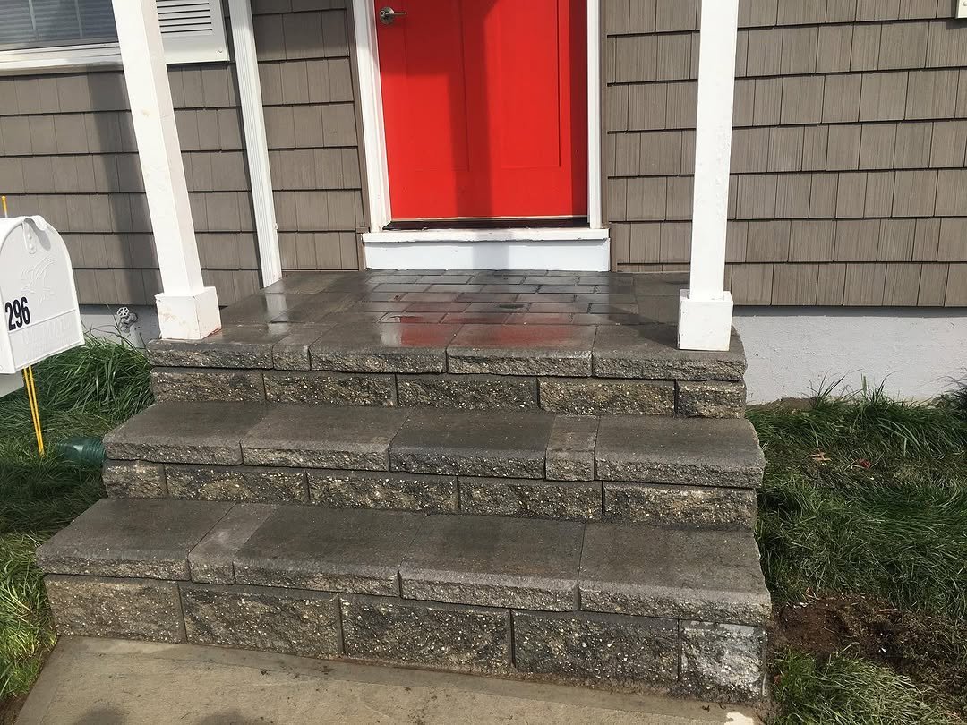 Stone steps leading to a front porch with a red door, surrounded by brown siding and white trim.