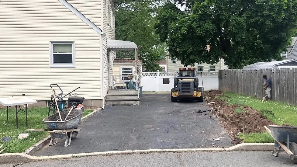 A driveway is being worked on with a small bulldozer, construction tools, and workers present