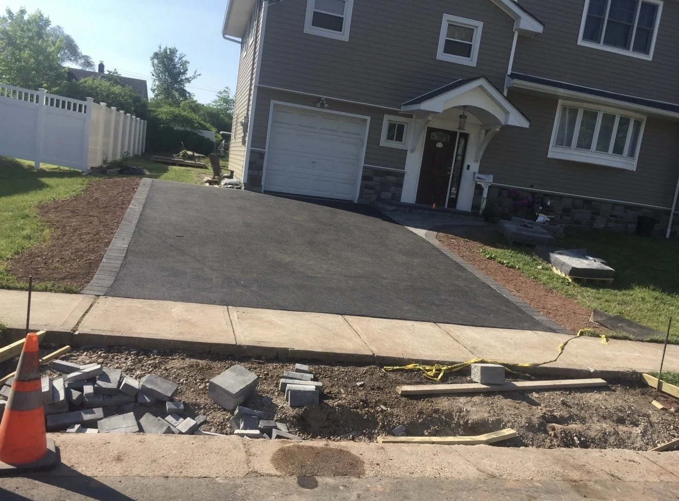 Front yard of a house under construction with new concrete sidewalk and driveway, construction tools, and orange safety cone.