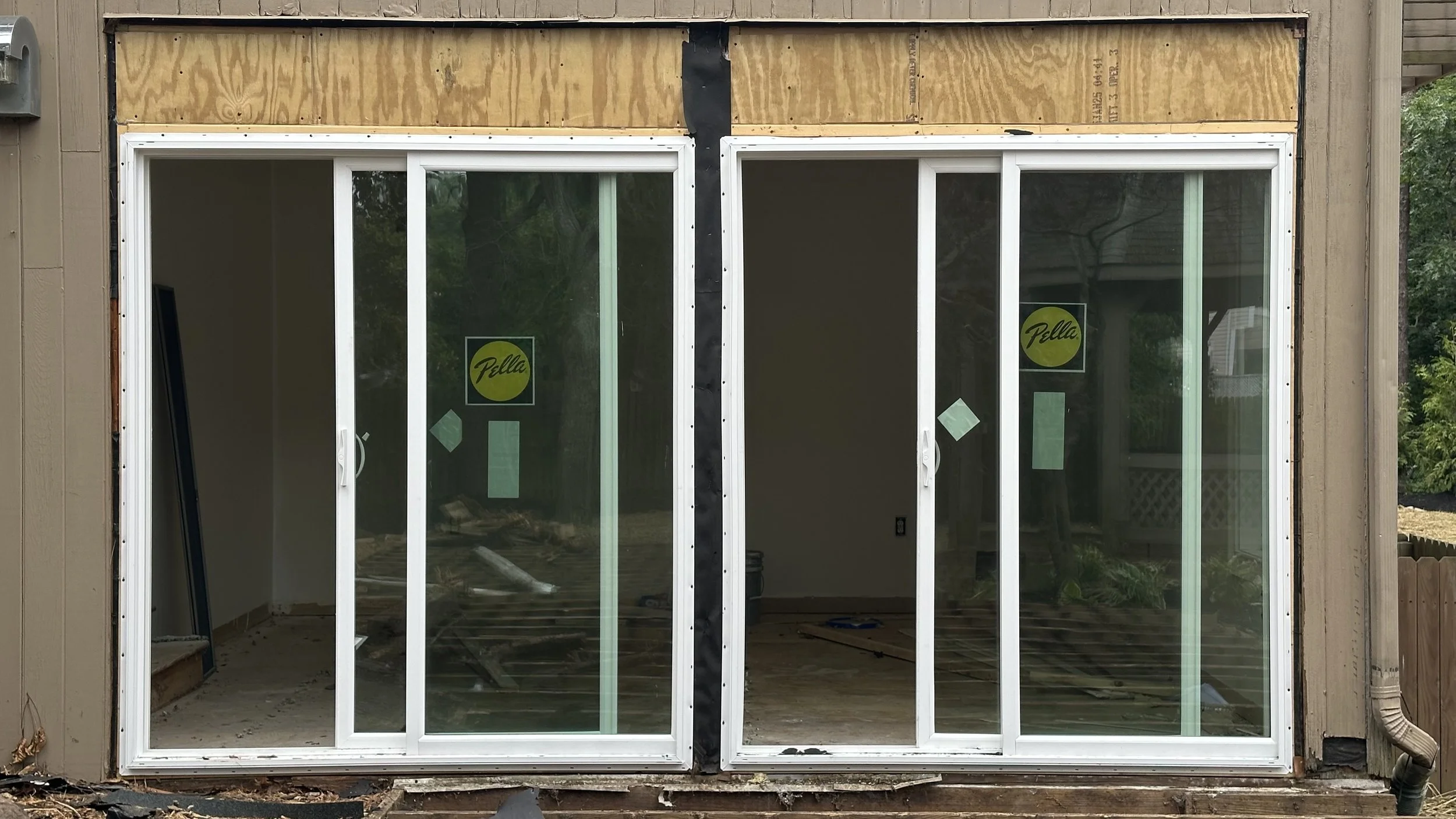 Sliding glass door installation in progress, with unfinished wooden frame and construction debris on the ground.