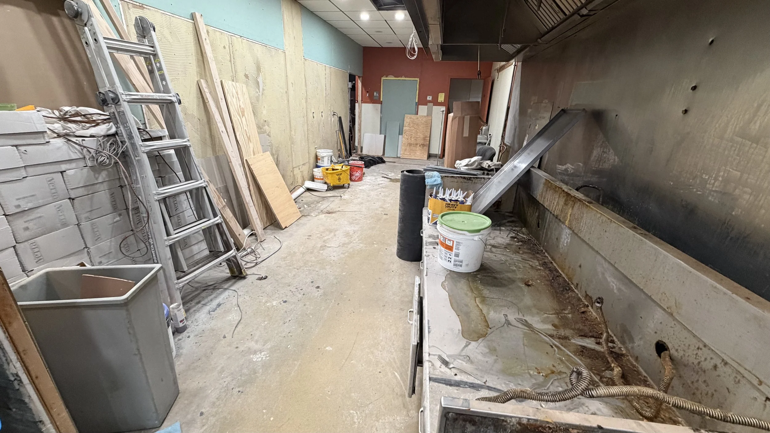 Construction or renovation room with tools, wood planks, ladders, buckets, and a dirty work sink.