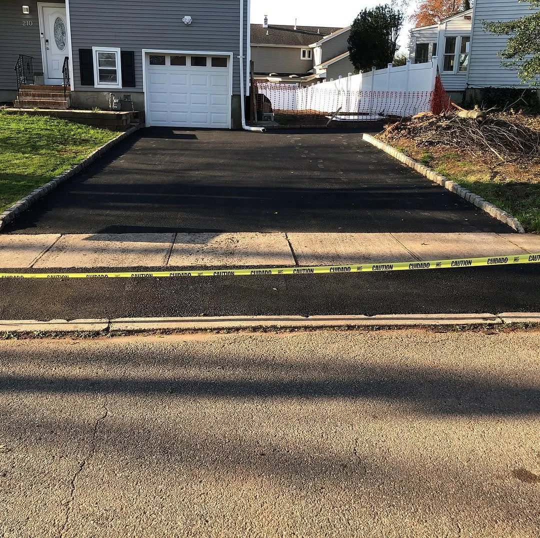 Newly paved driveway with caution tape across the sidewalk in front of a house.
