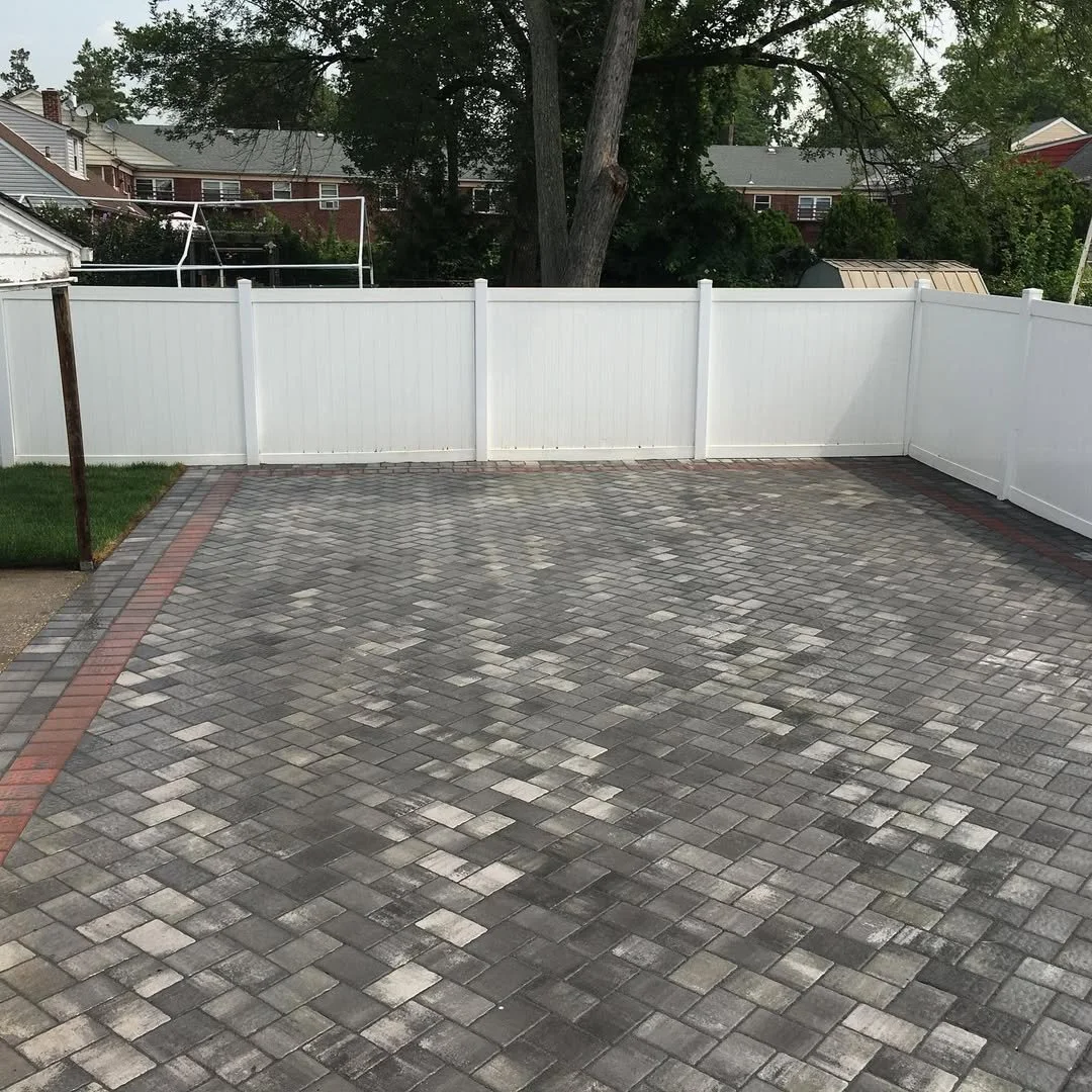 Clean paved backyard with gray stone tiles, white privacy fence, and a tree in the background.