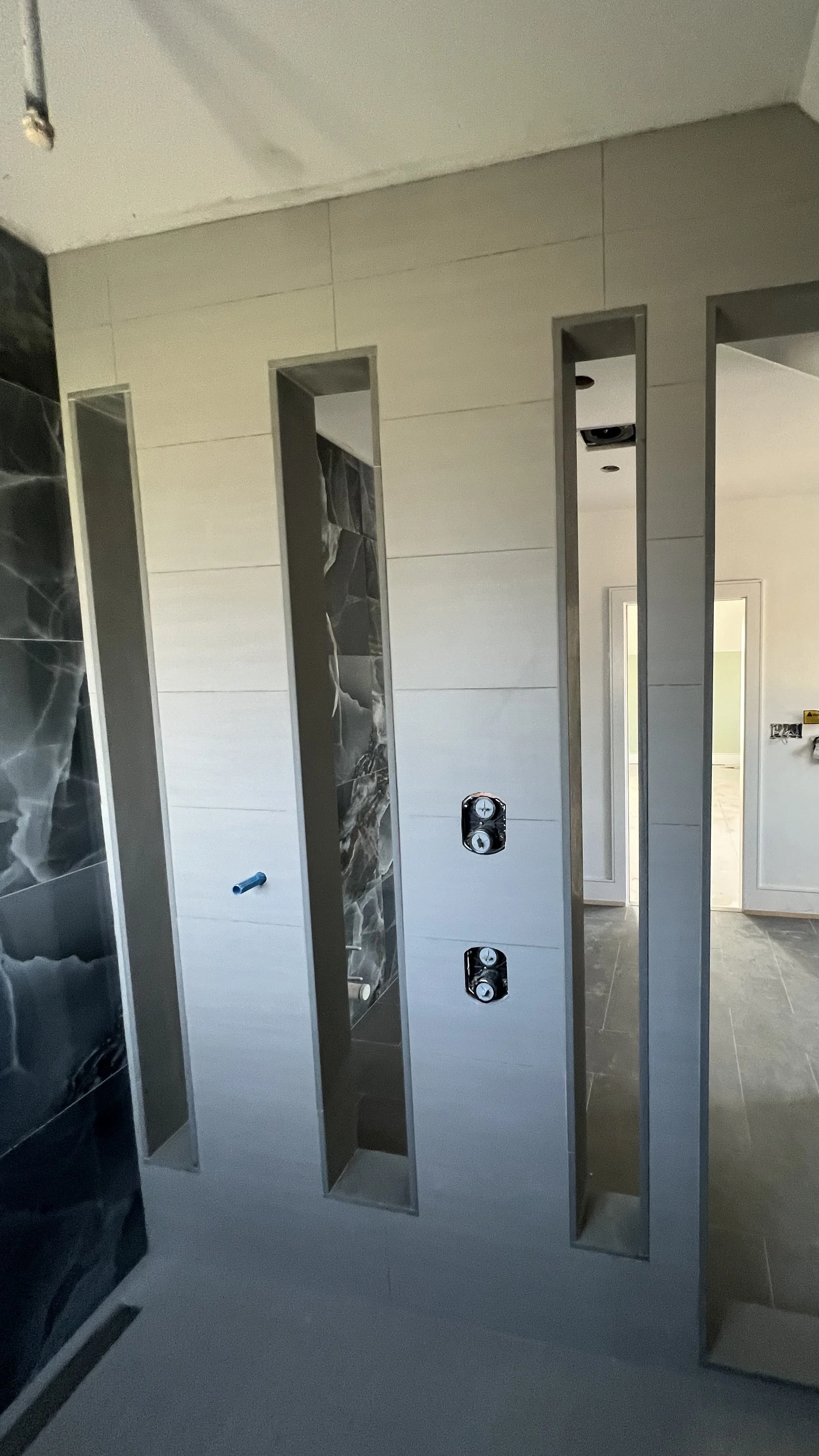 Photo of a bathroom under construction with partially installed tiles and fixtures, including wall outlets and openings for plumbing.