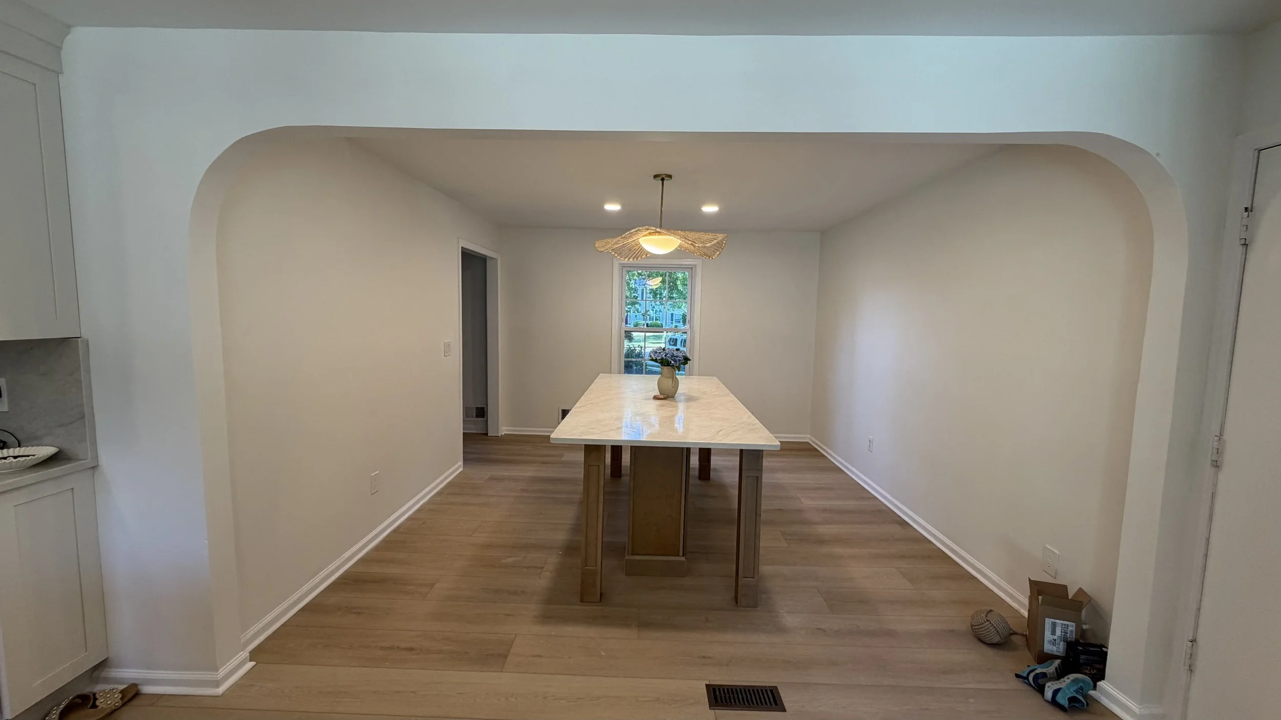 Empty dining area with a rectangular marble-top table, a decorative pendant light, and a window with a view of greenery outside.