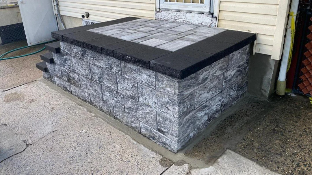 Stone and brick outdoor step with a black border, located next to a house with yellow siding and a door.