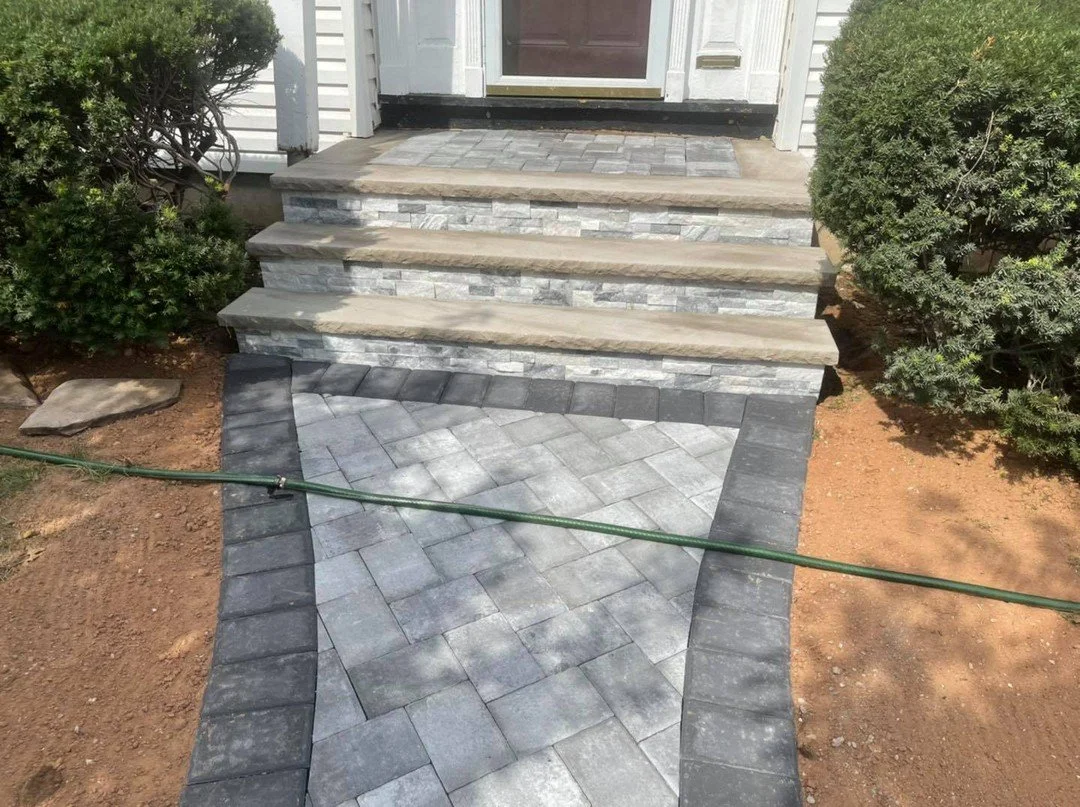 Front steps and walkway with new stone and pavers leading to a front door, flanked by bushes, with soil on either side.