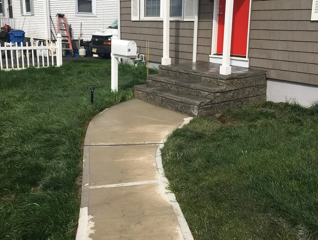 Concrete walkway leading to front steps of a house with a red door.