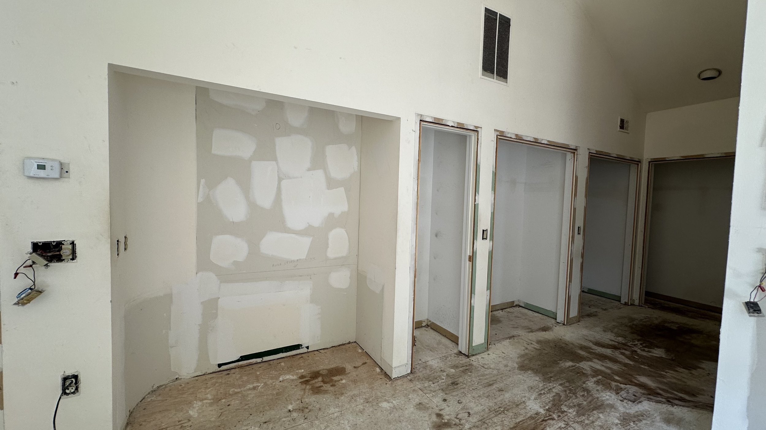 Interior of a room under renovation with drywall patches on the walls, unfinished door frames, and a stained floor.