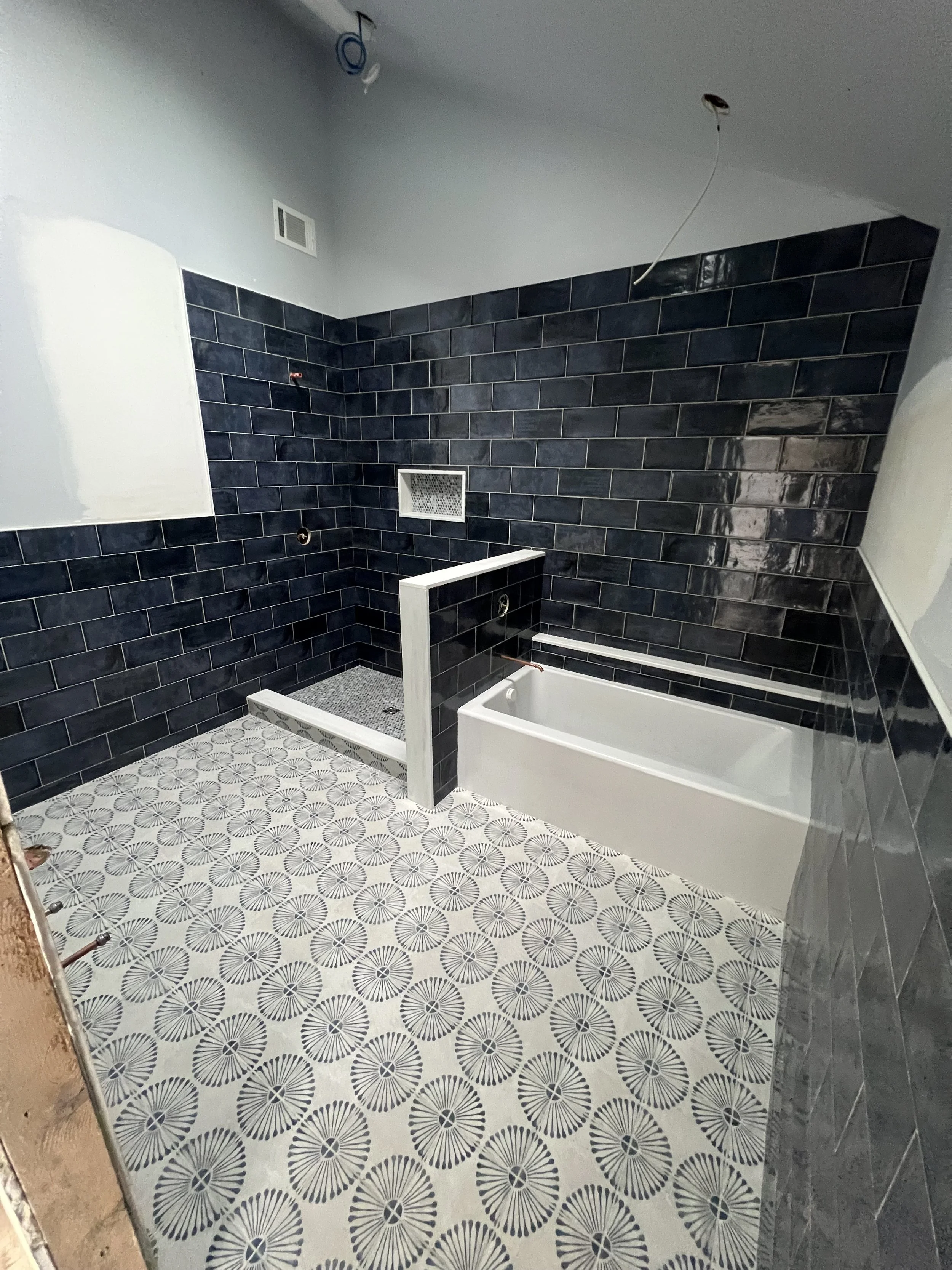 Bathroom under renovation with black subway tile walls, patterned floor tiles, a bathtub, and exposed wiring.