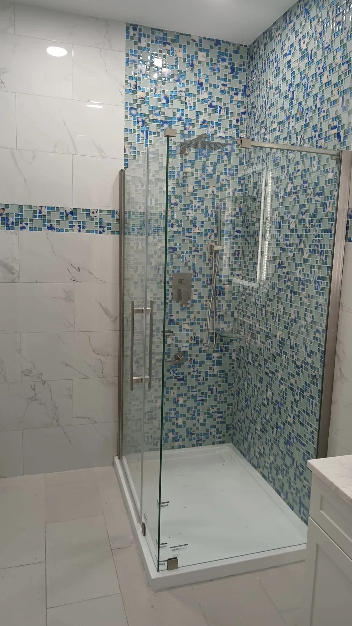 A modern bathroom shower with clear glass enclosure, blue mosaic tile walls, and a rain showerhead.