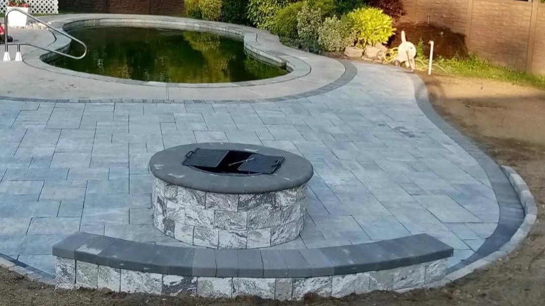 A backyard with a fire pit, patio paving, a swimming pool, garden plants, and outdoor decor.