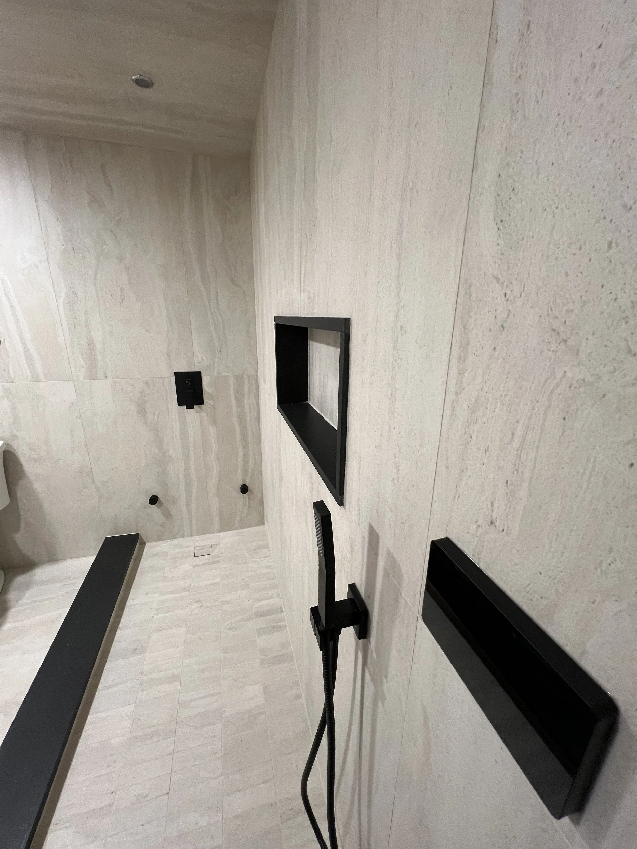 Interior of an empty modern room with beige stone walls and floor, black rectangular shelves, and black wall sockets.