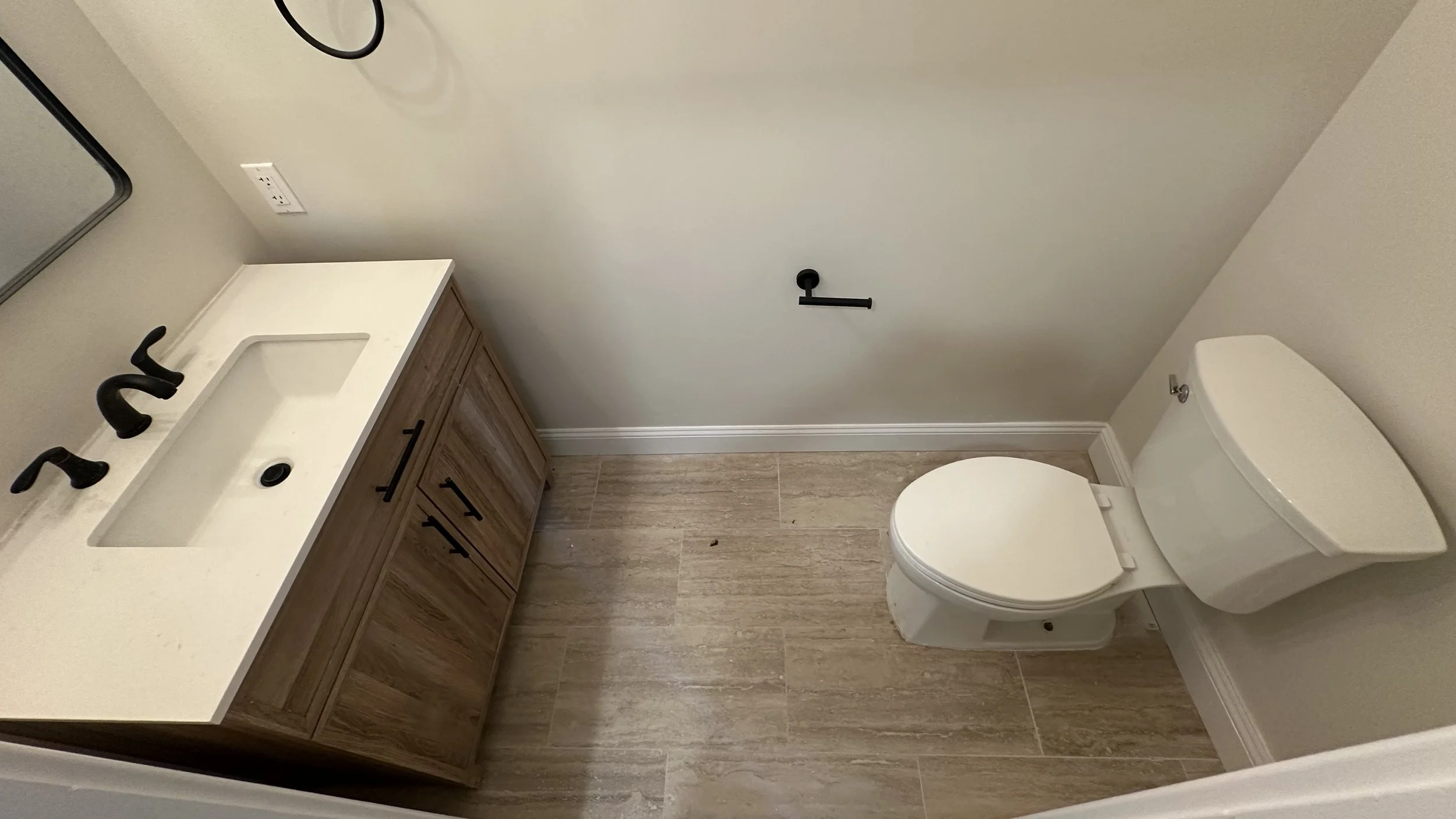 Empty bathroom with a wooden vanity with a white countertop and black fixtures, a mirror, a toilet, and a towel holder on the wall.