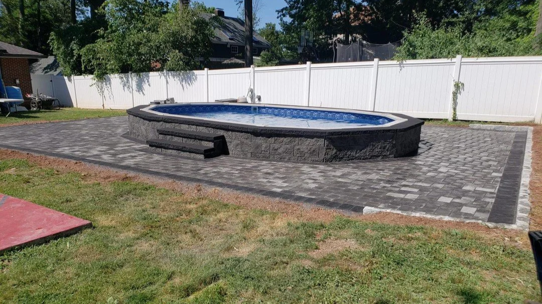 Backyard with in-ground pool surrounded by gray pavers and fenced yard.