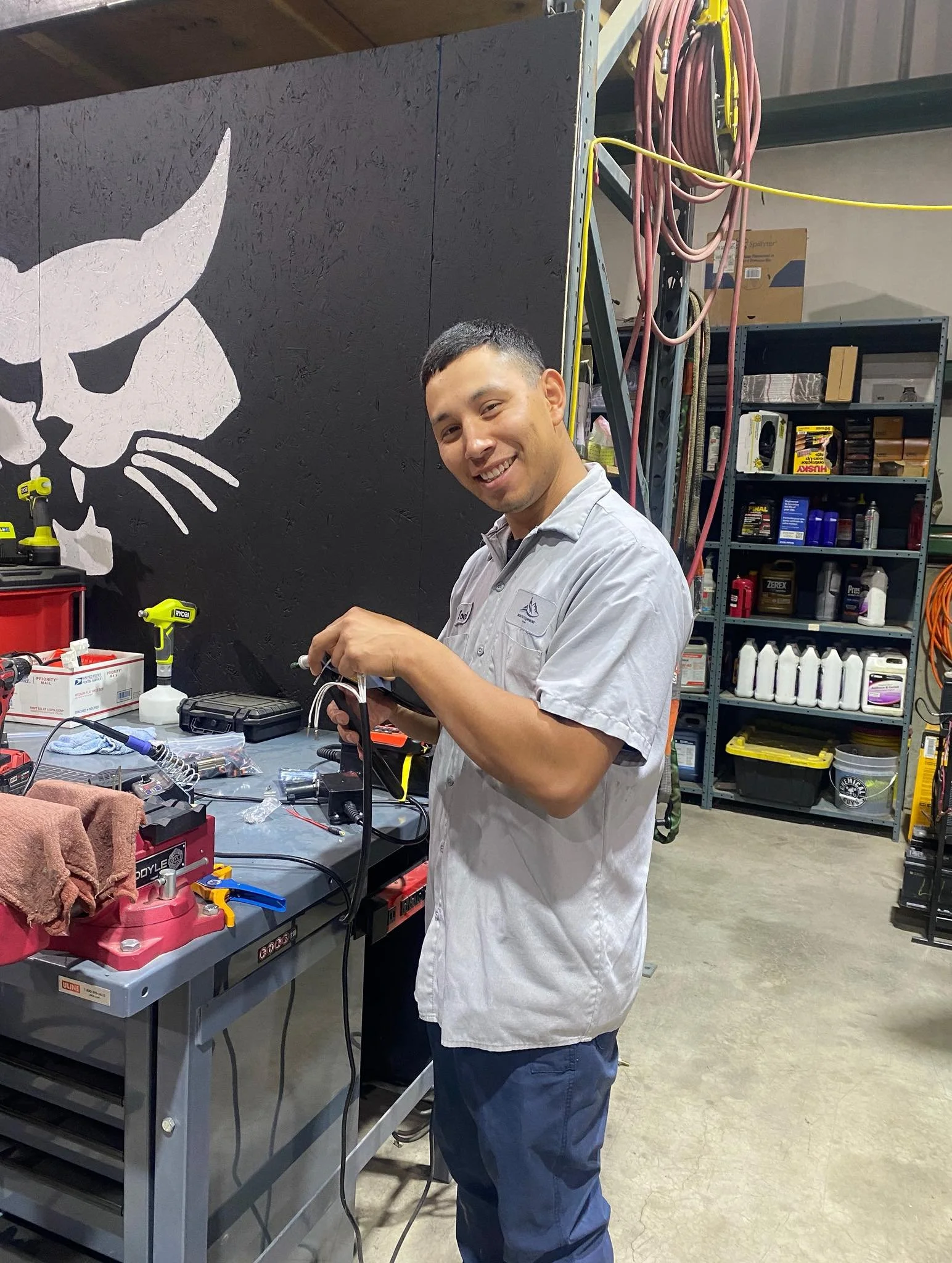 A man smiling, working with electronic devices at a workbench in an industrial workshop.