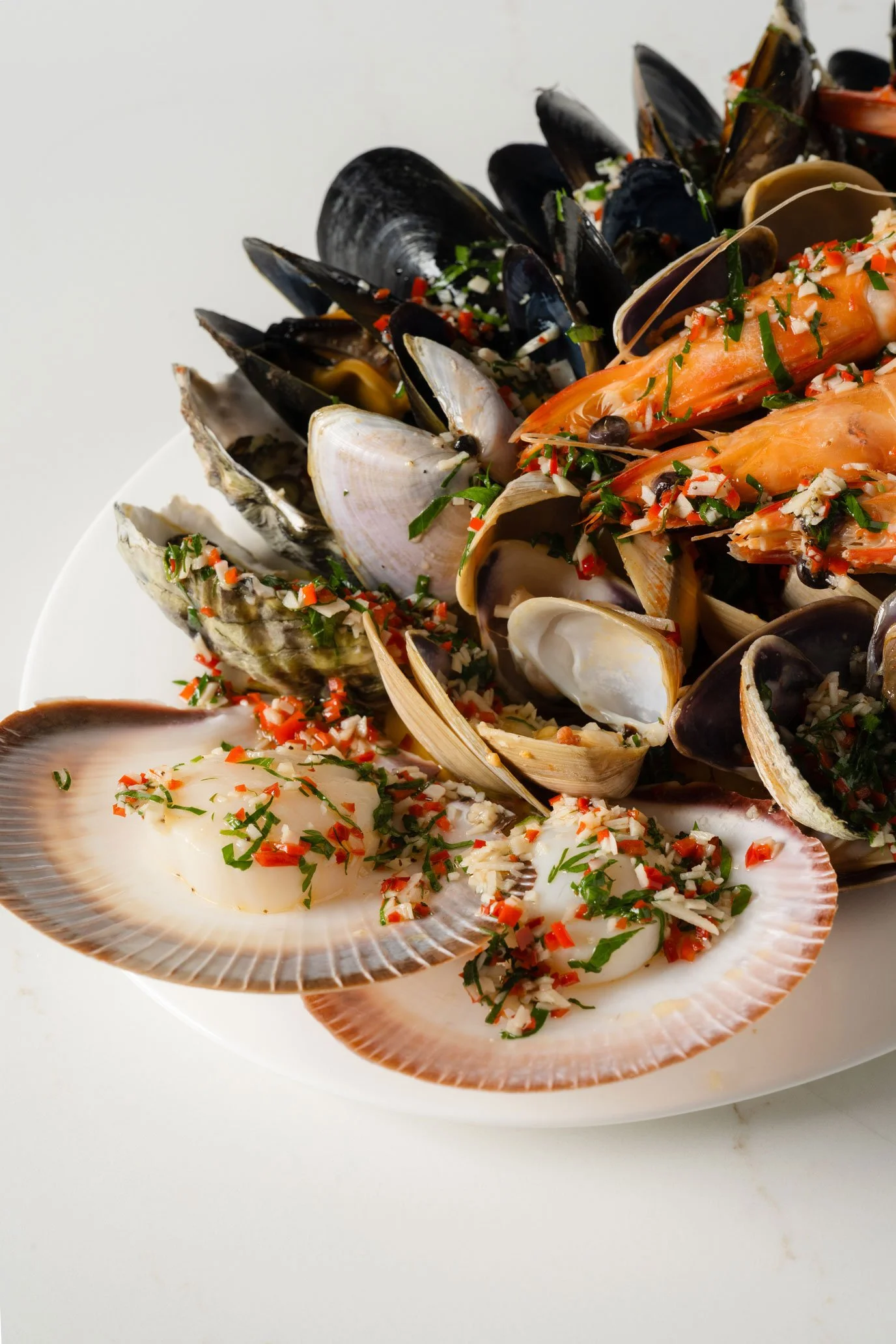 Seafood platter with mussels, clams, shrimp, and scallops garnished with chopped herbs and red pepper flakes