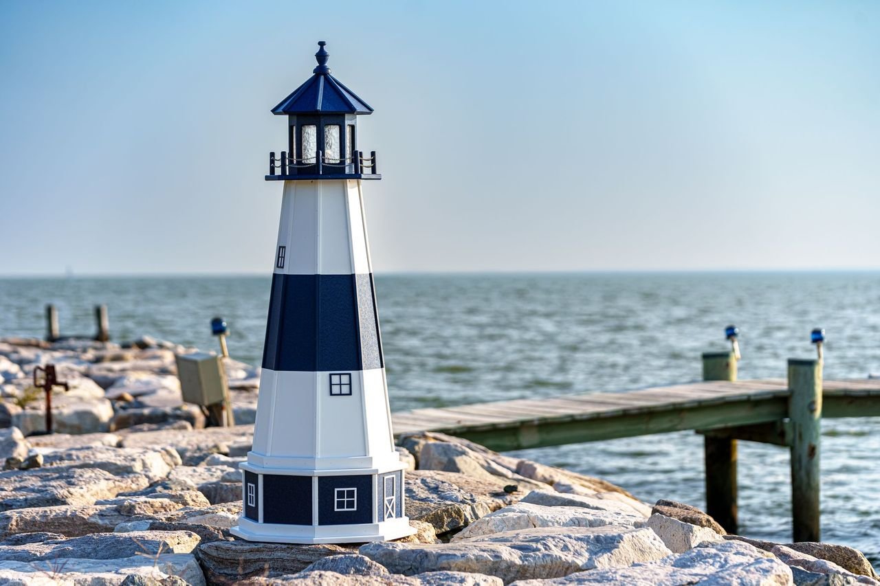 Model lighthouse on rocky shore with water and sky in background