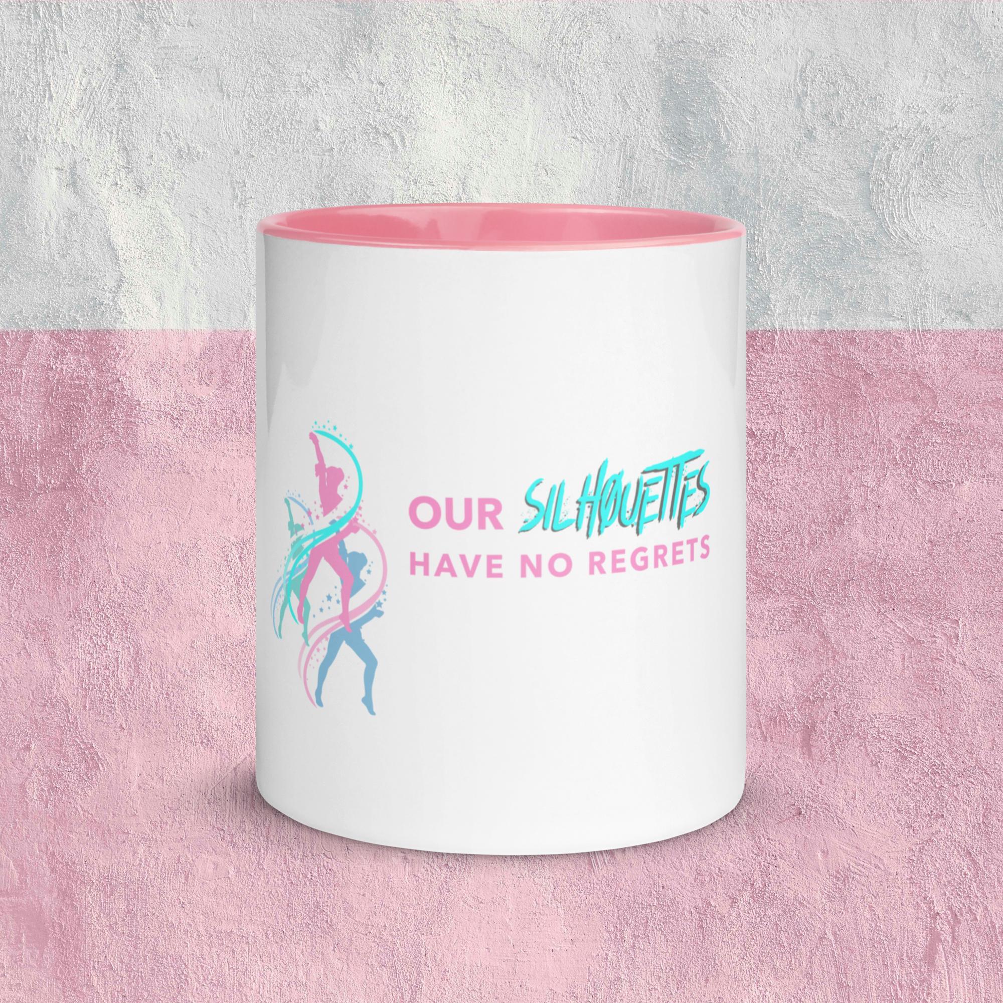 A white mug with pink interior and a colorful fitness-themed design and text that reads "Our Silhouettes Have No Regrets" in front of a two-toned pink and gray textured background.