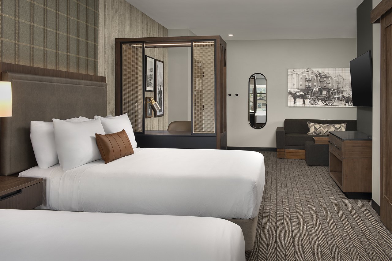 Modern hotel room with a sleeping area, seating, and a small adjoining area with a desk and glass partition.