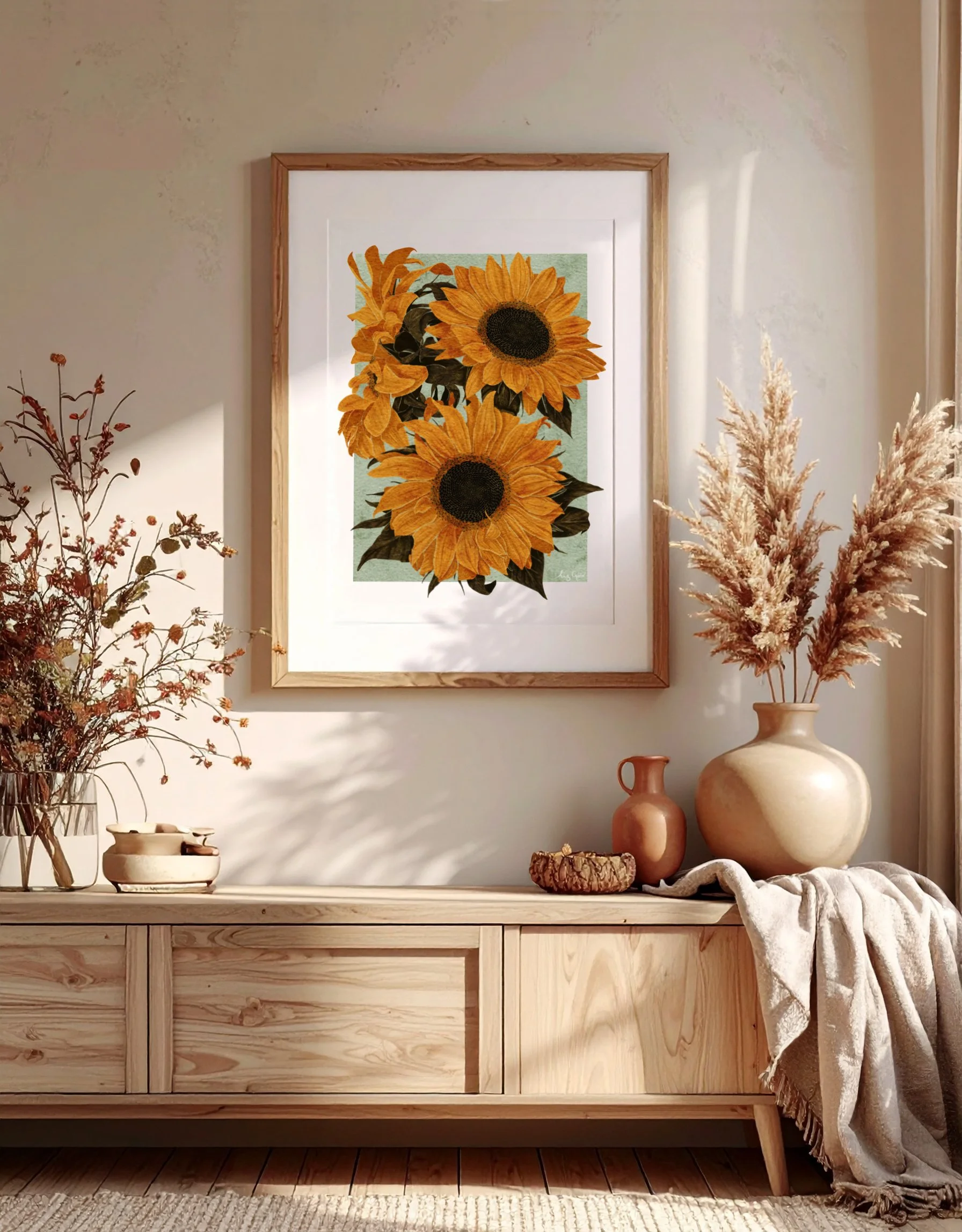 Sunflowers art print by Liz Govier displayed above a wooden sideboard with dried stems and ceramic vessels.
