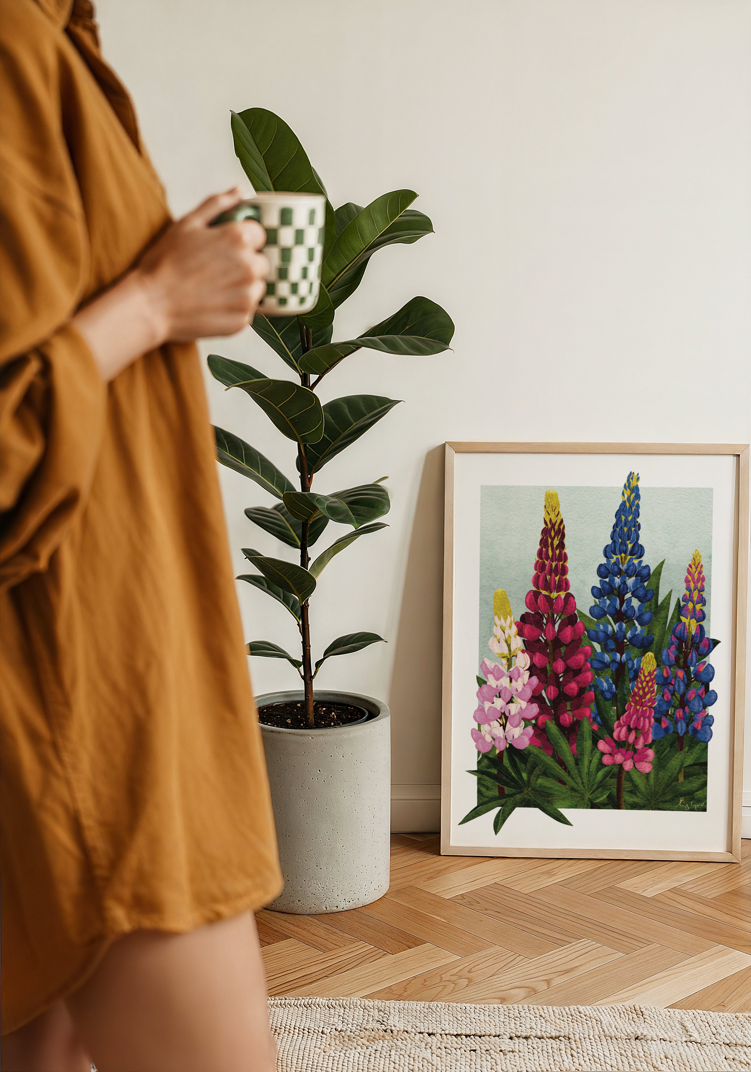Framed Lupins fine art print by Liz Govier Studio resting against a wall beside a potted plant and morning light.