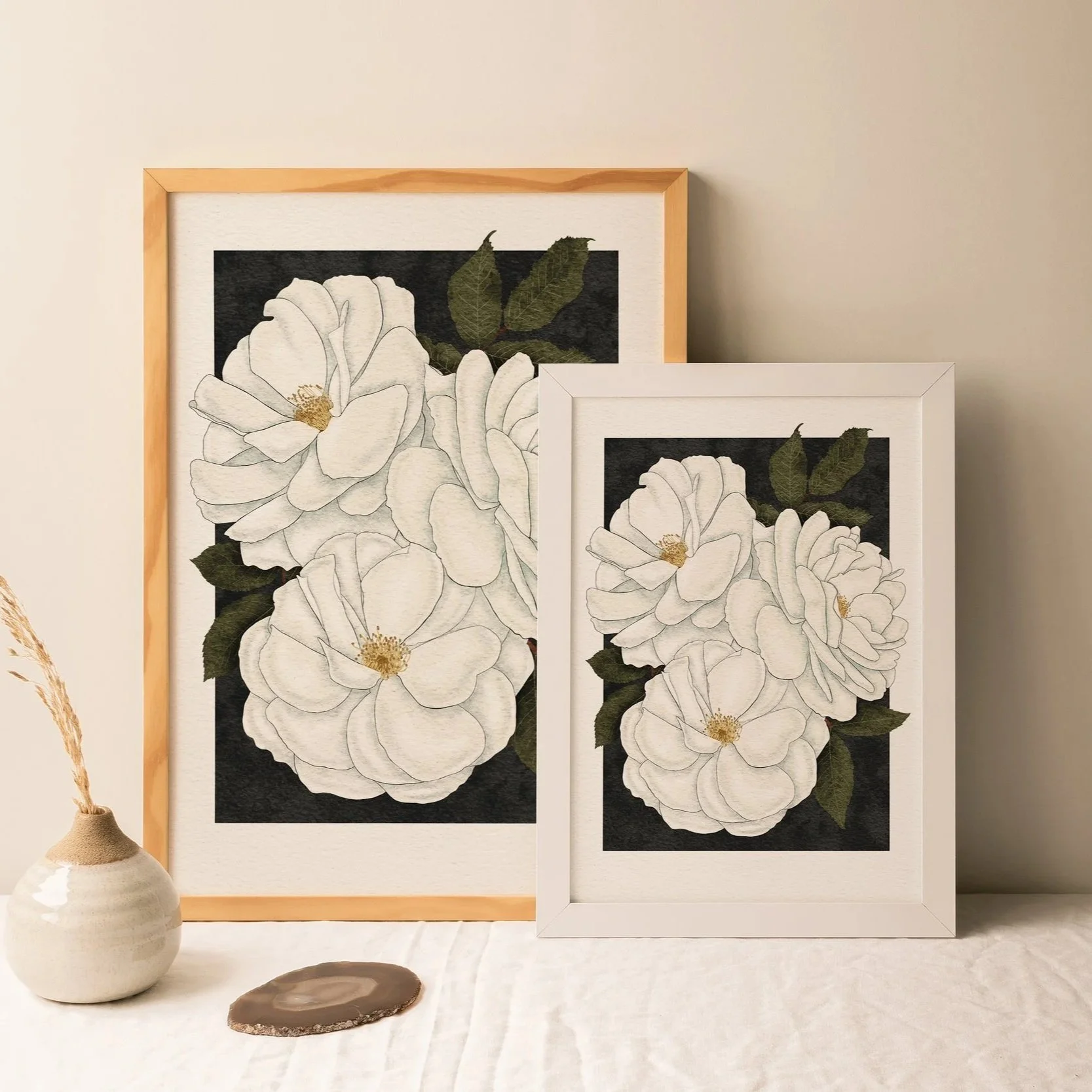 Two sizes of Madame Alfred Carrière roses art prints framed in white and light wood, styled together on a linen-covered surface with ceramic vase, botanical wall art by Liz Govier Art Studio.