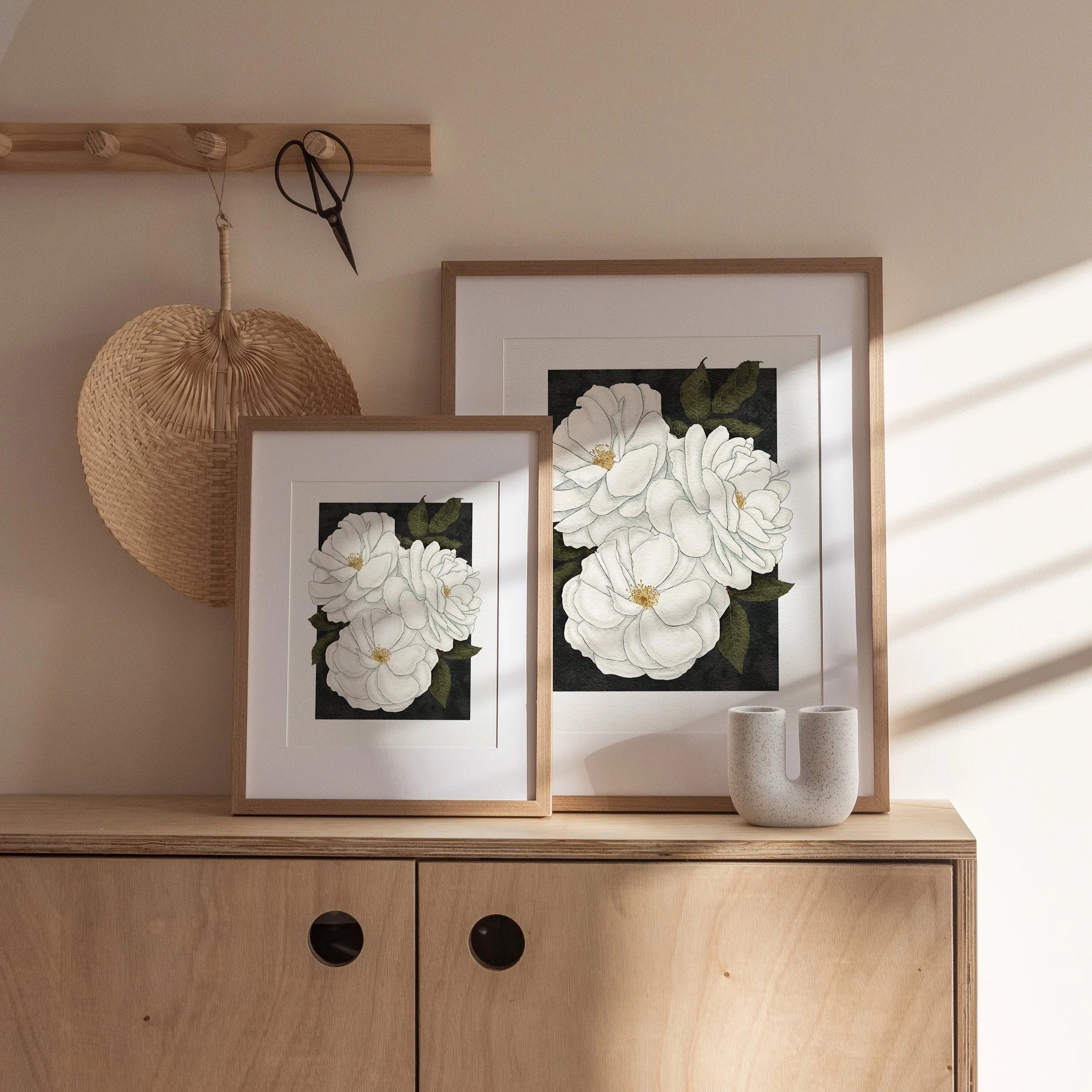 Pair of framed Madame Alfred Carrière roses art prints displayed on a wooden cabinet with ceramic vase, botanical wall art by Liz Govier Art Studio.