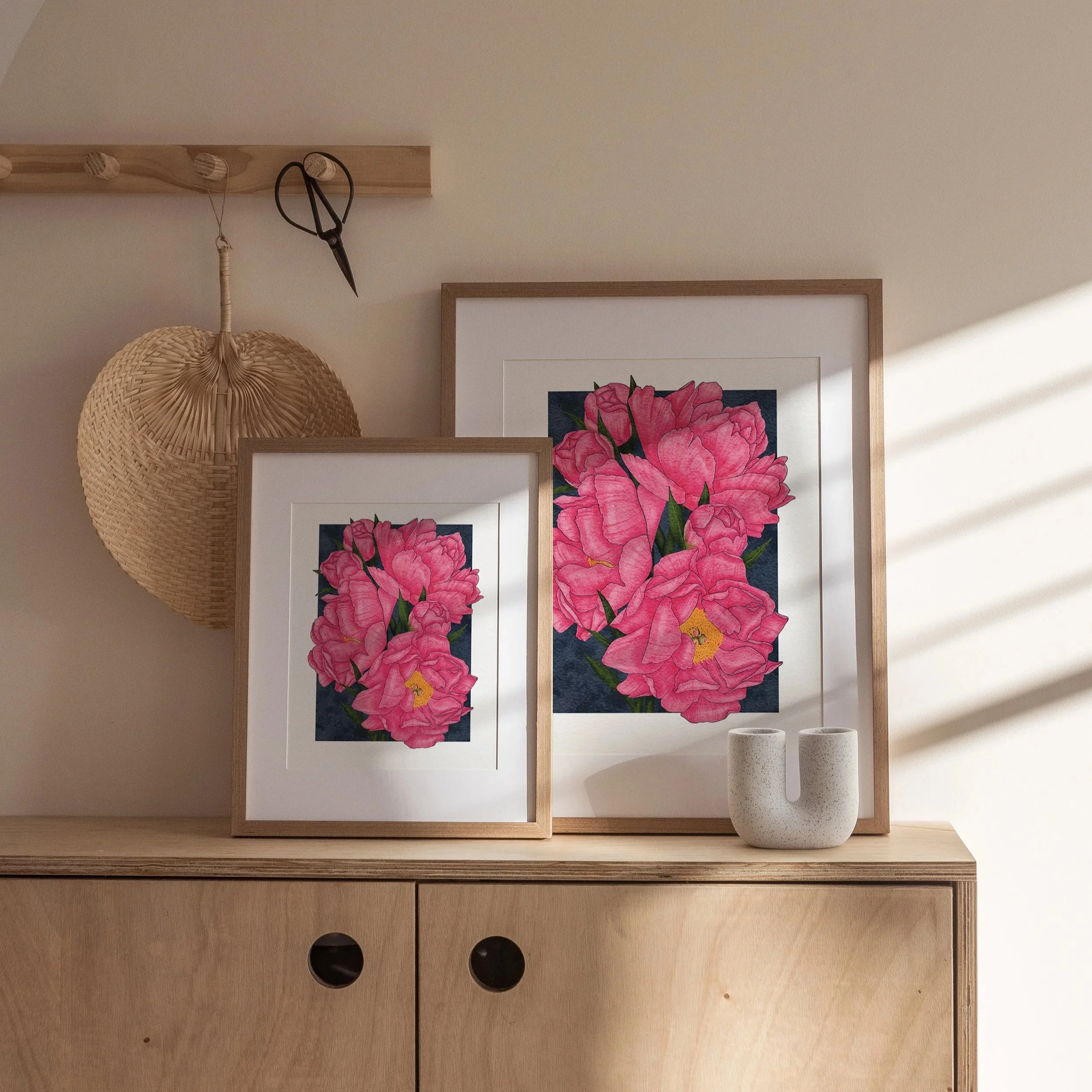 Pair of Karl Rosenfield Peonies art prints in white and wood frames, displayed on a wooden cabinet in soft natural light, luxury botanical wall art.