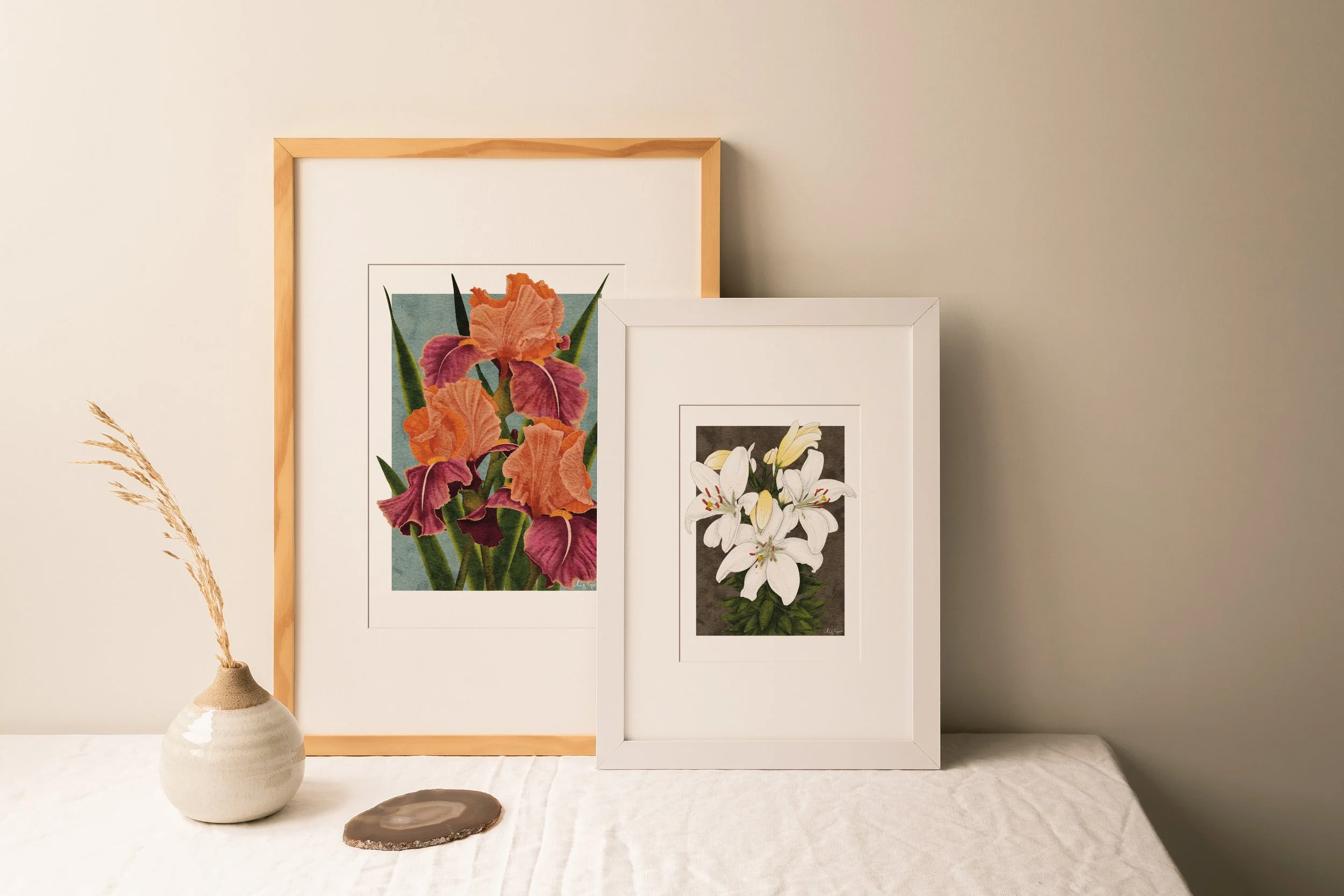 Two framed botanical fine art prints by Liz Govier Studio — Carnaby Iris and White Lilies — styled together on a linen-covered sideboard with soft neutral decor.