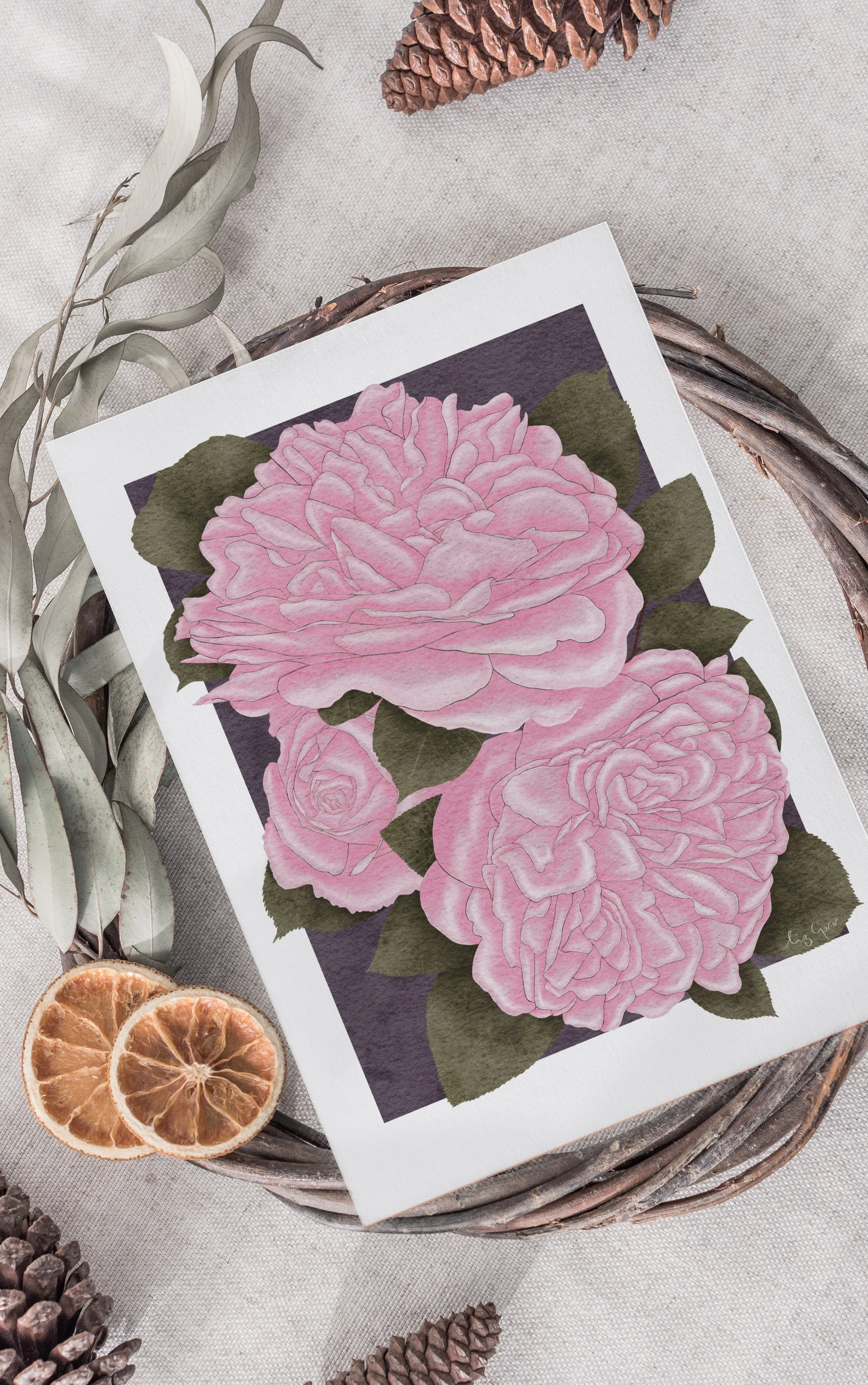 Pink Roses fine art print laid flat among pinecones, dried citrus, and winter foliage on a linen background.