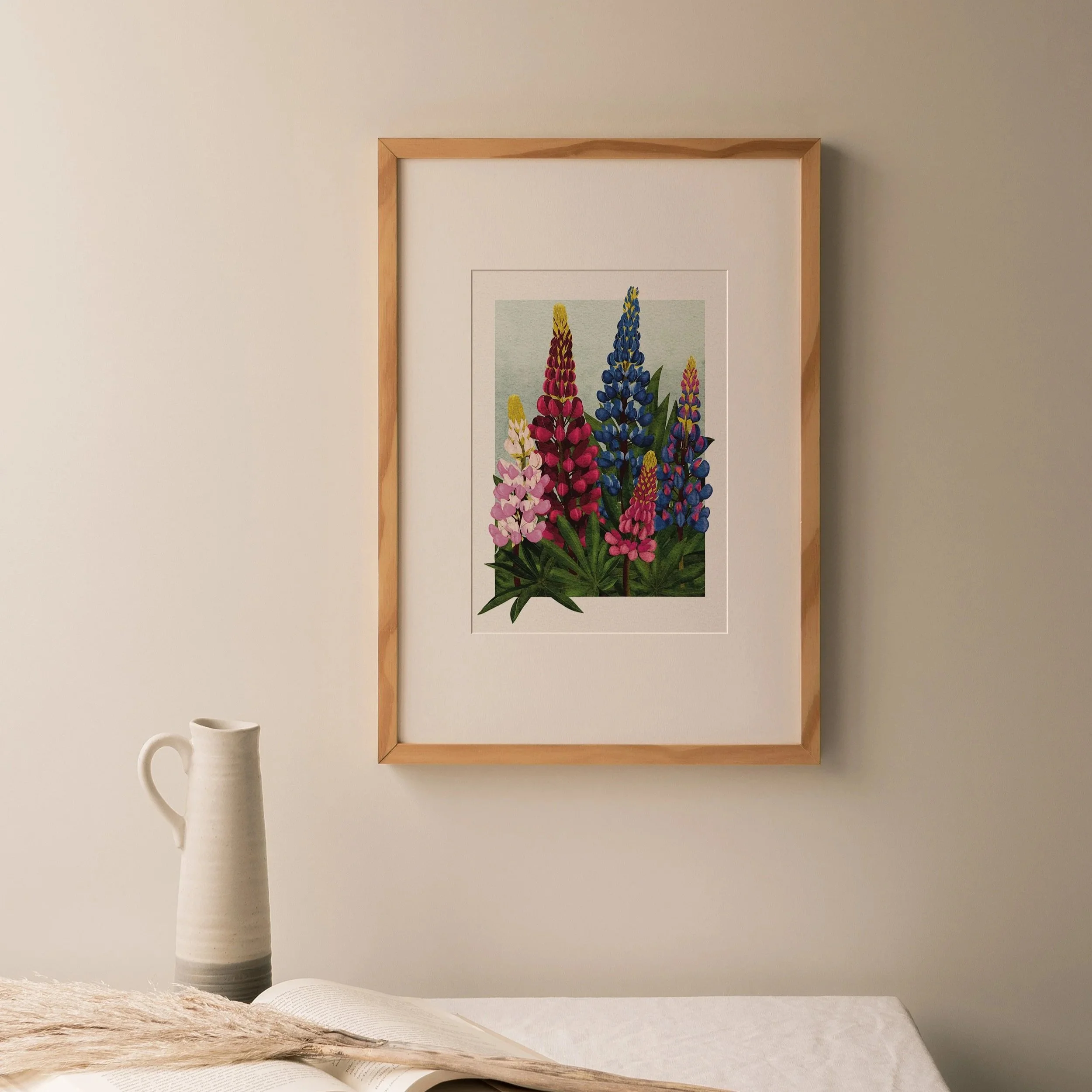 Lupins art print by Liz Govier Art Studio, digital botanical illustration of tall pink, red, and blue lupin flowers, framed in light wood and styled on a linen-draped table.