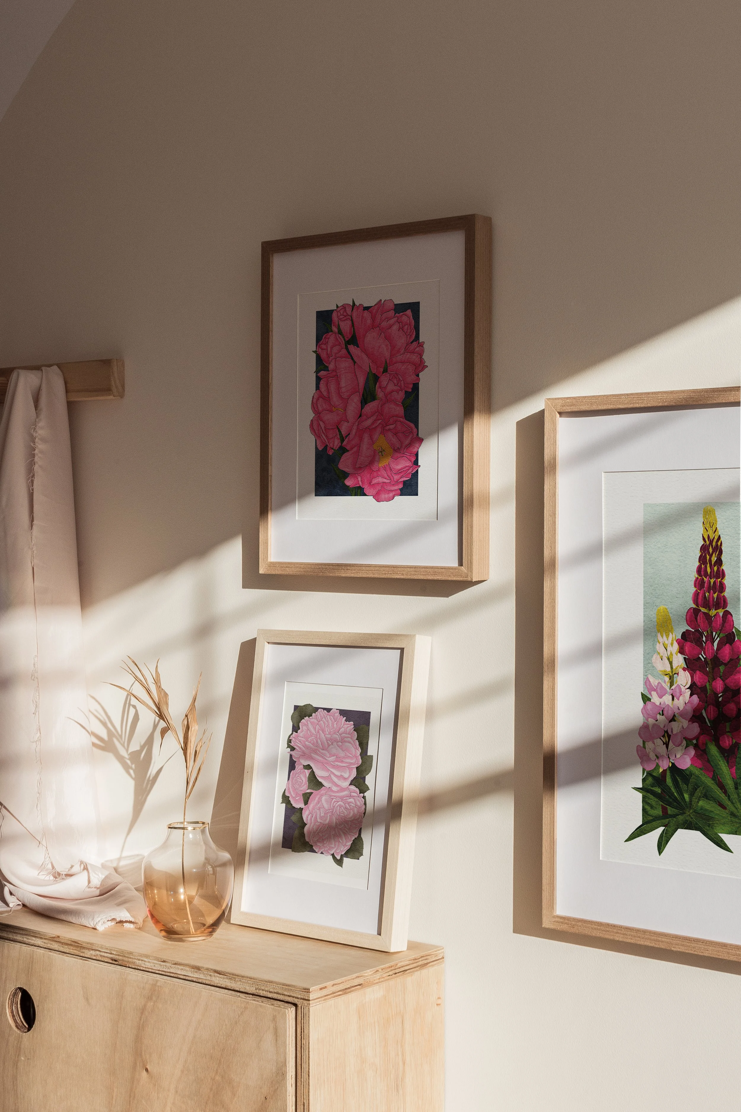 Framed Pink Roses, Karl Rosenfield Peonies, and Lupins art prints by Liz Govier in natural light on a wooden cabinet.