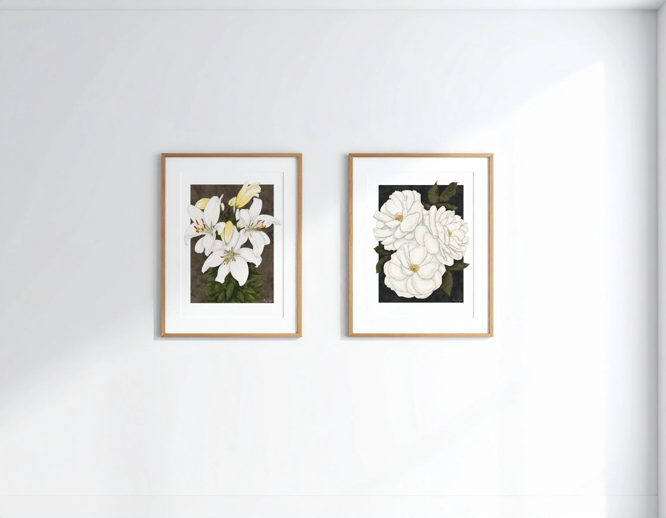 Two framed botanical fine art prints by Liz Govier Studio — White Lilies and White Roses — displayed side by side on a softly lit wall.