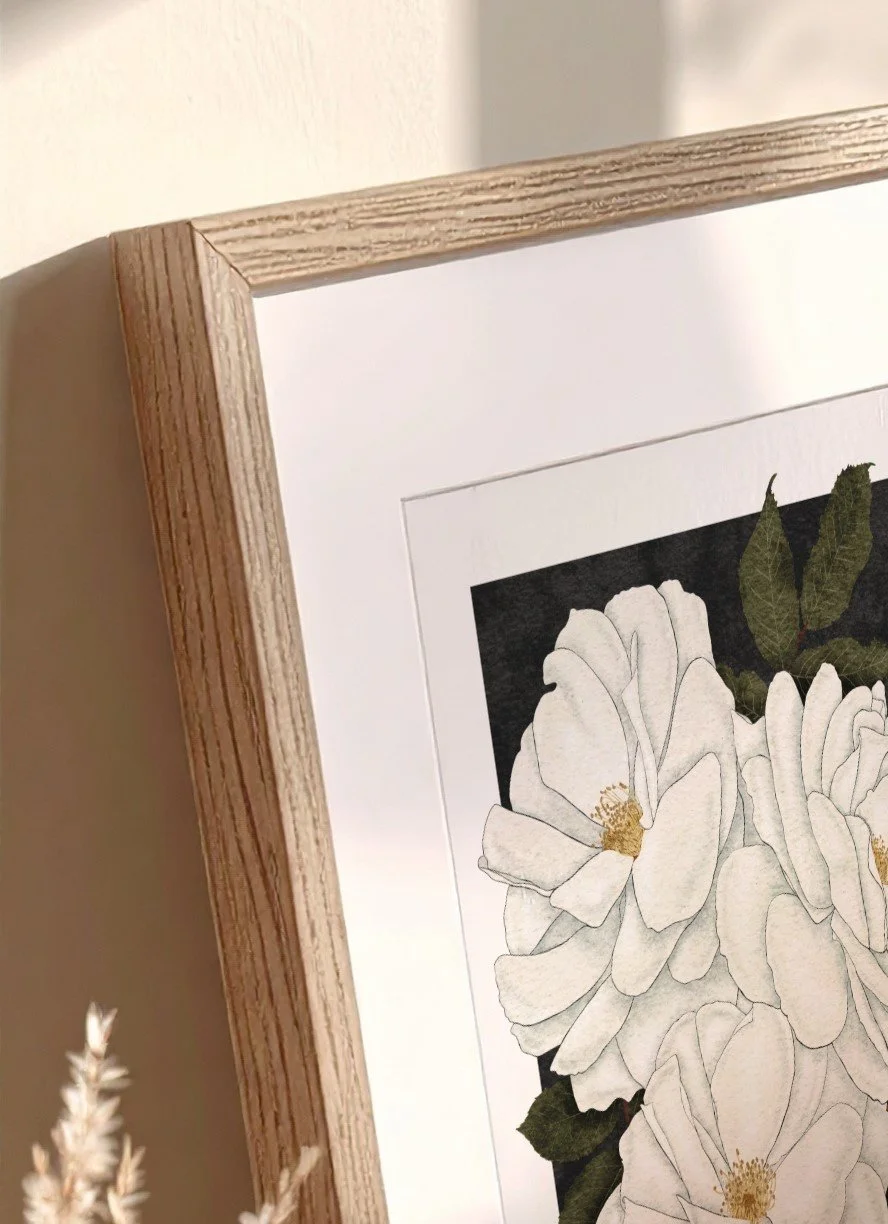 Close-up of Madame Alfred Carrière fine art print by Liz Govier Studio in a natural oak frame, showing the soft white petals and deep green leaves in morning light.
