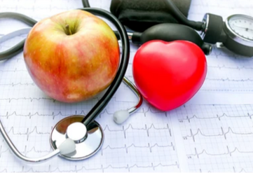 An apple, a red heart-shaped object, a stethoscope, and an blood pressure cuff on an electrocardiogram monitor.